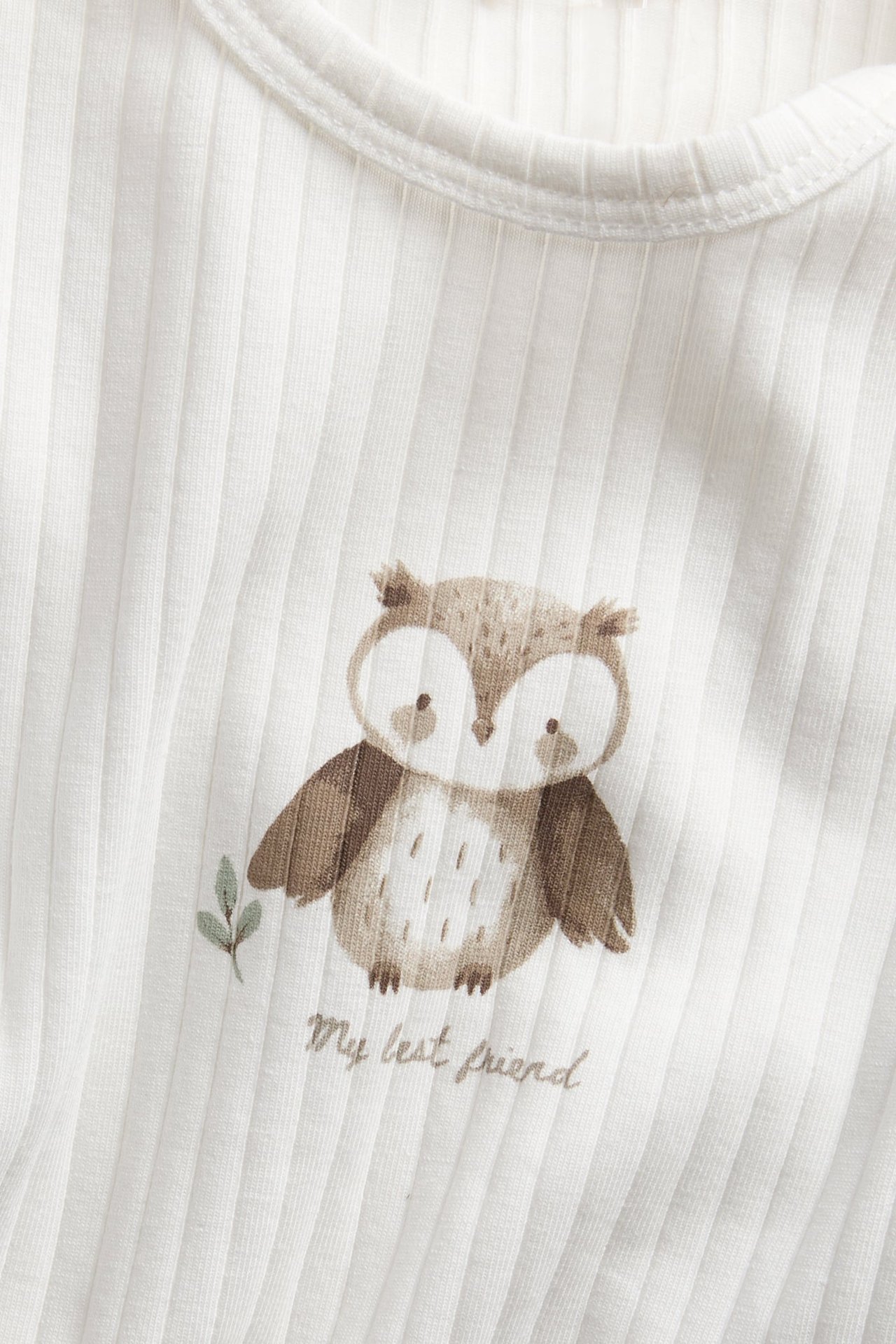 Nahaufnahme eines weißen gerippten Baby-Tops mit braunem Eulendruck und "My best friend" Schriftzug.