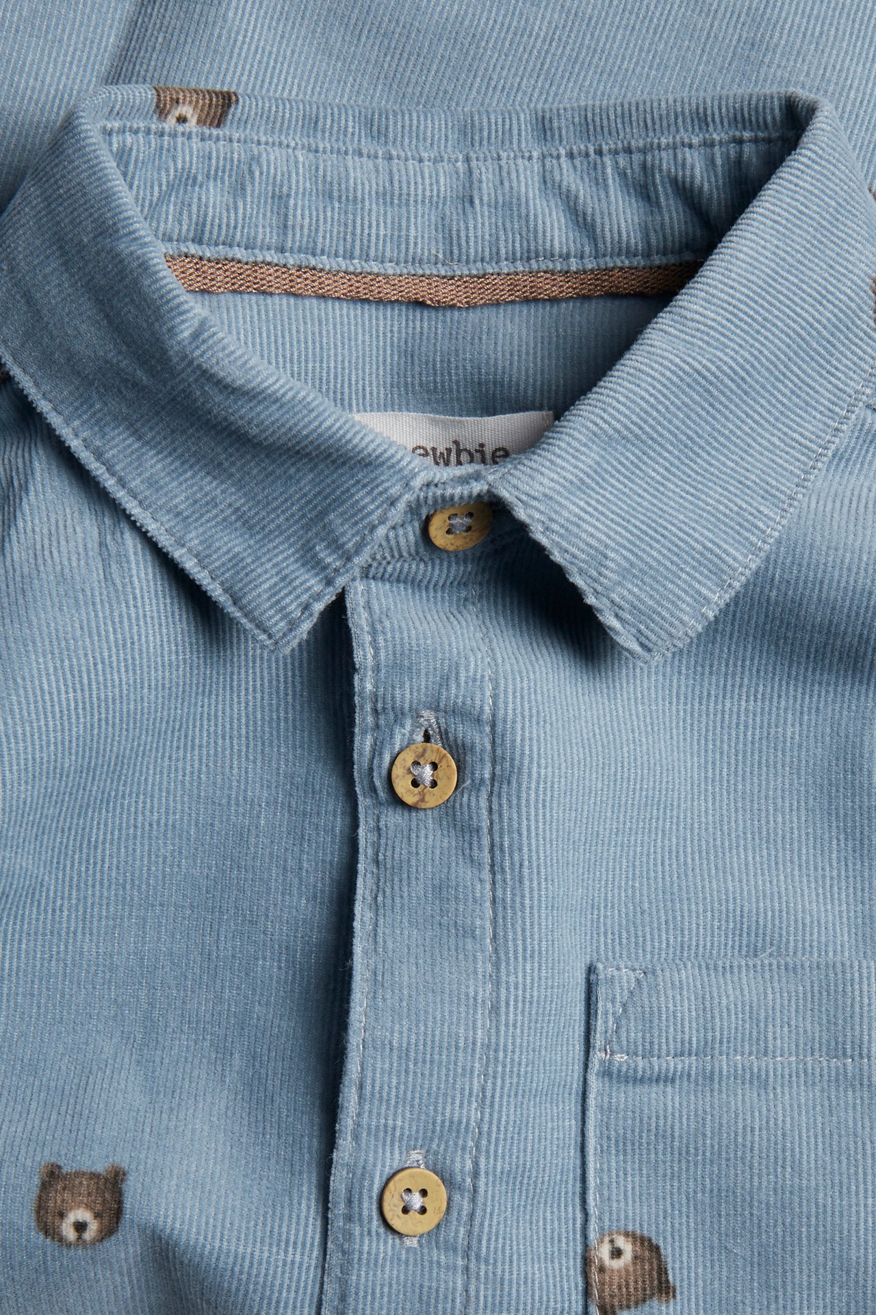 Close-up of a light blue corduroy baby shirt with bear print and wooden buttons.