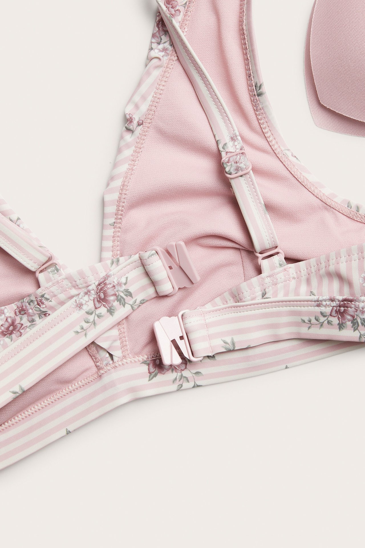 Close-up of a women's pink and white striped floral bikini top with adjustable straps and a back clasp.