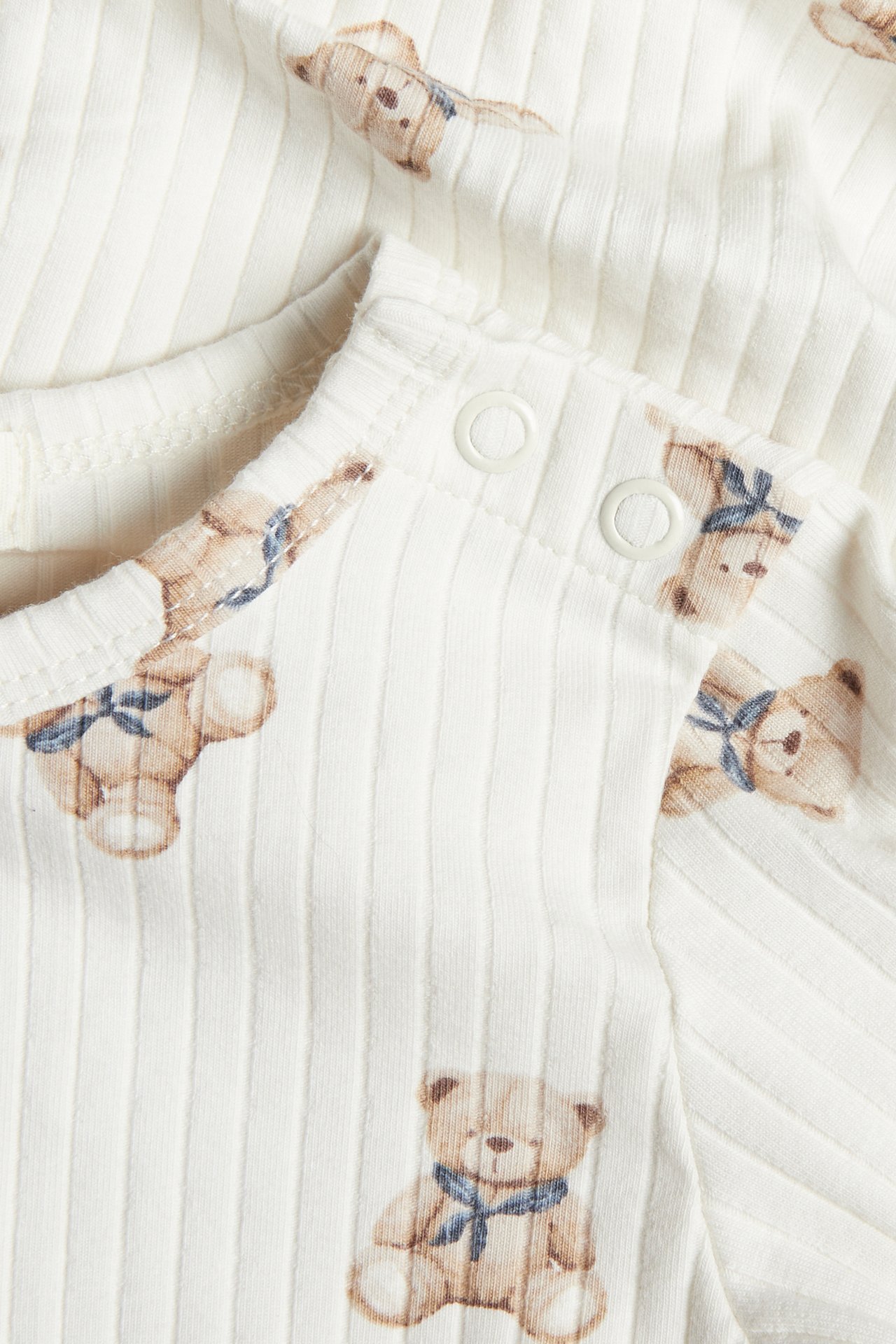 Close-up of a baby's ribbed white long-sleeved top with a teddy bear print and shoulder snap buttons.