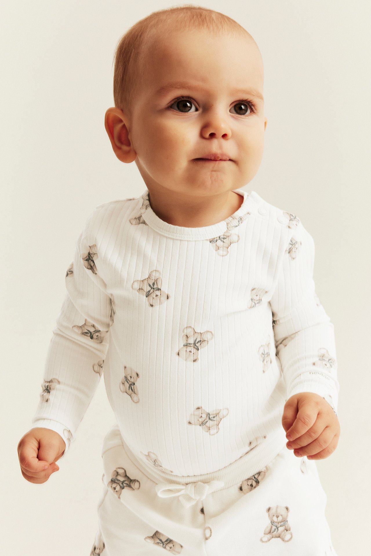 Front view of a baby wearing a white ribbed long-sleeve top with teddy bear print and matching pants.