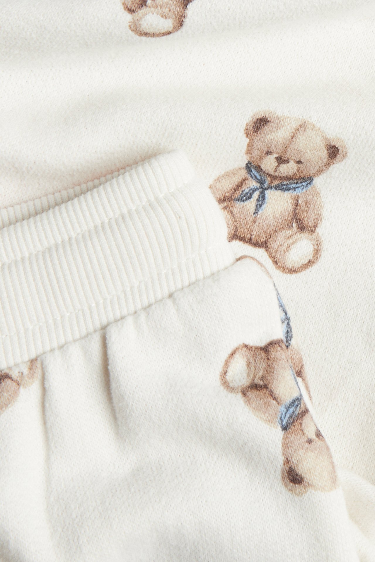 Close-up of cream baby sweatpants with an allover teddy bear print and a ribbed waist.