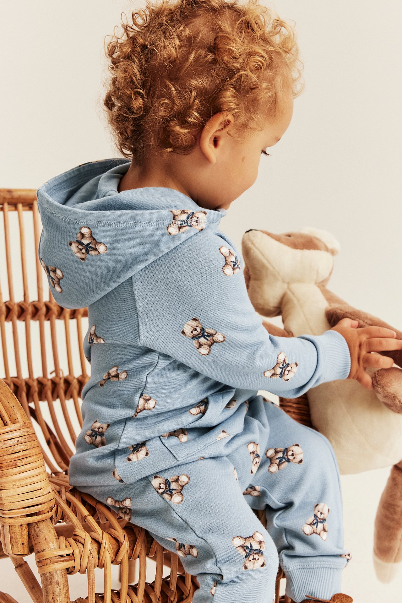 Back view of baby wearing a light blue teddy bear print hoodie and matching sweatpants, holding a plush toy.