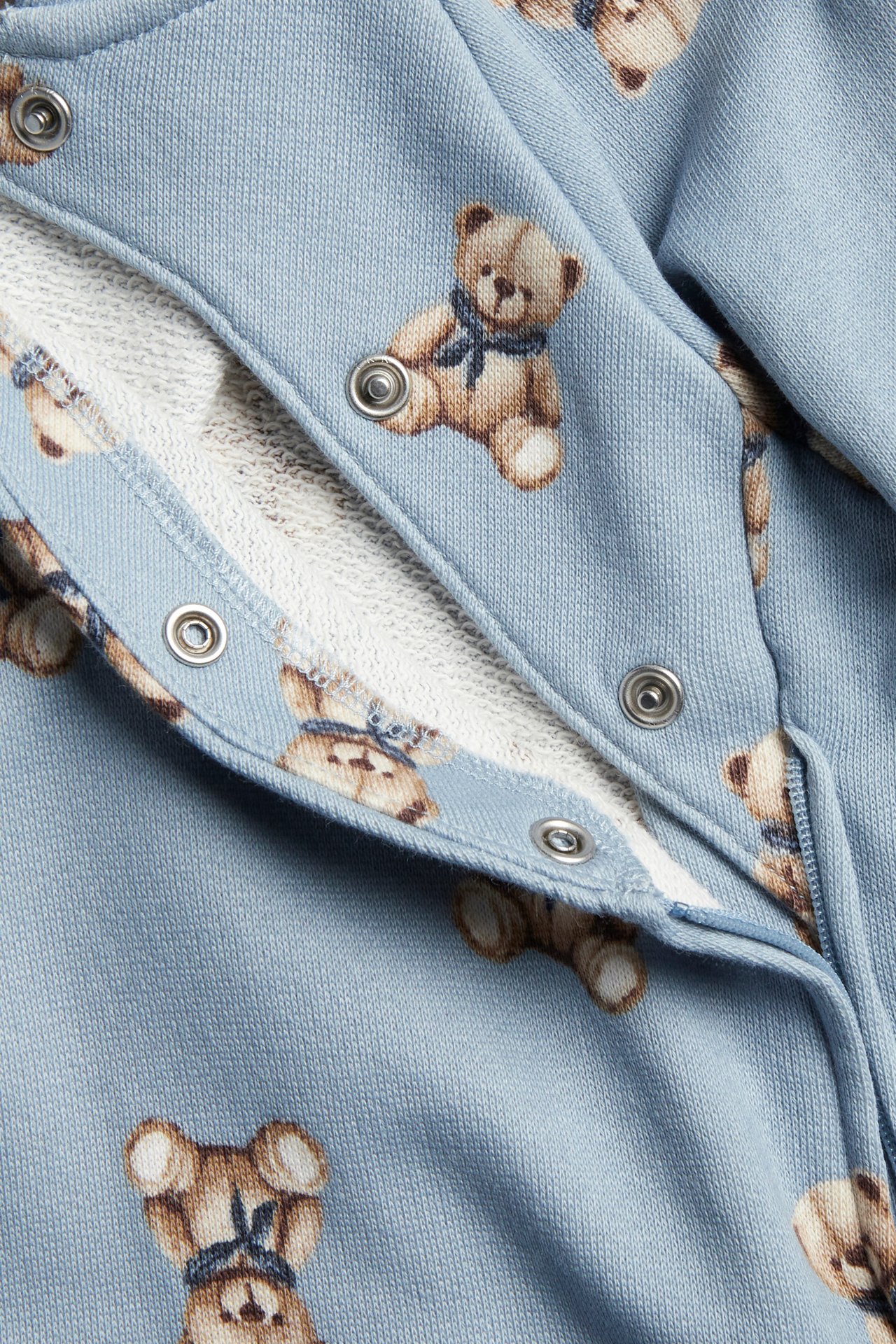 Close-up of a baby's light blue teddy bear print romper with snap button fastening.