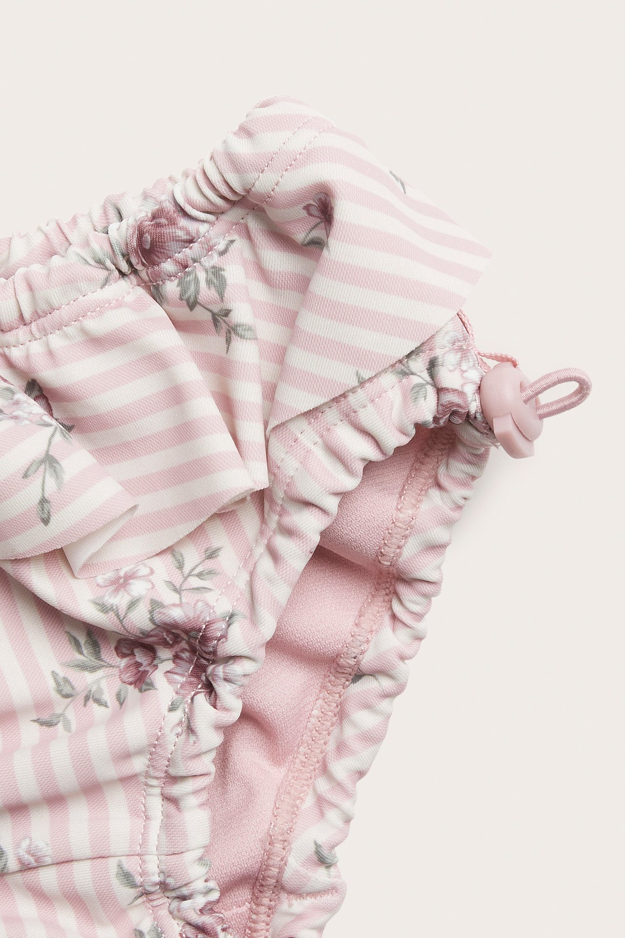 Close-up of pink and white striped floral baby swim shorts with ruffles and a drawstring.