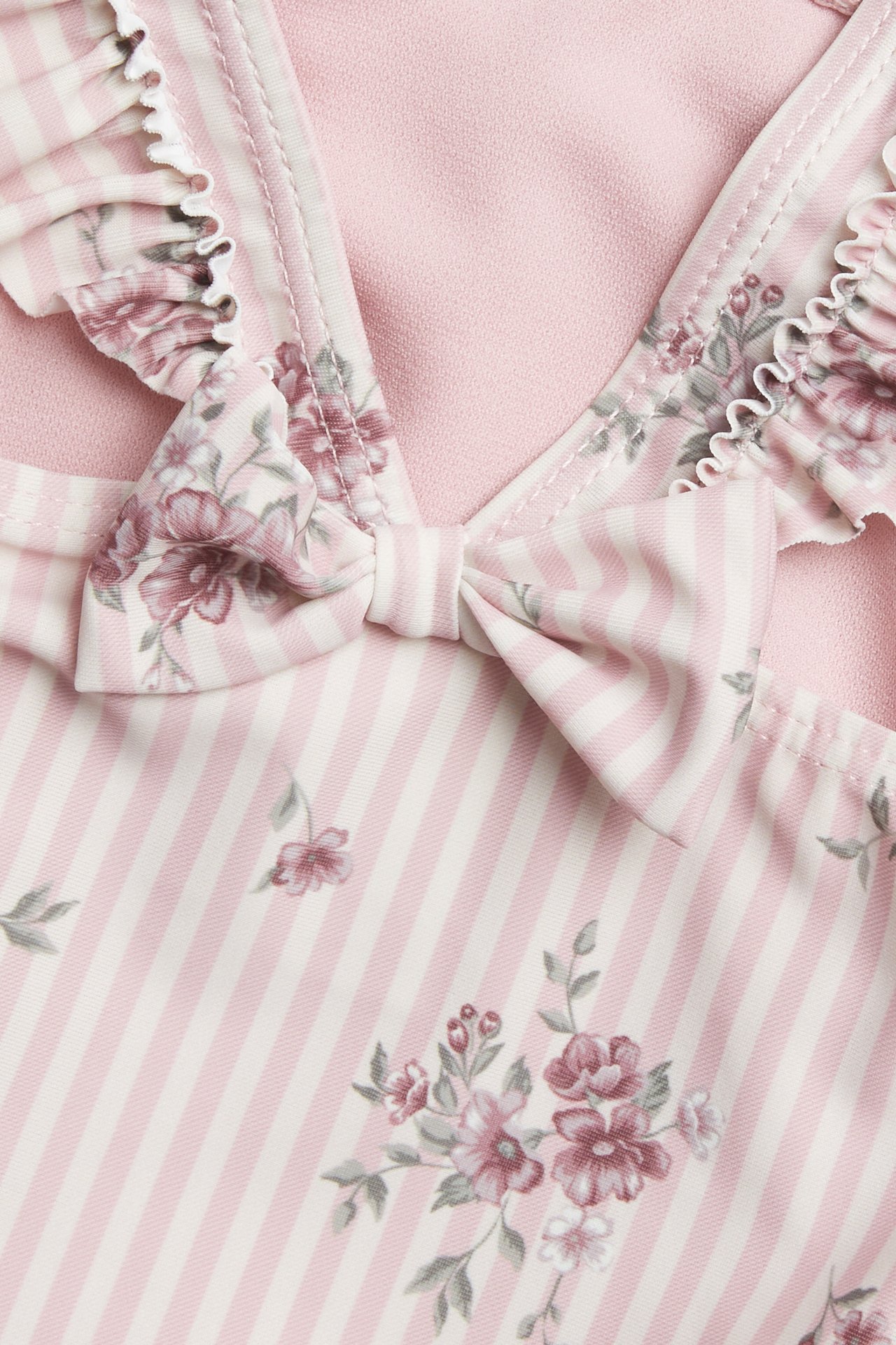 Close-up of a kid's pink and white striped swimsuit with floral print, ruffles, and a bow.