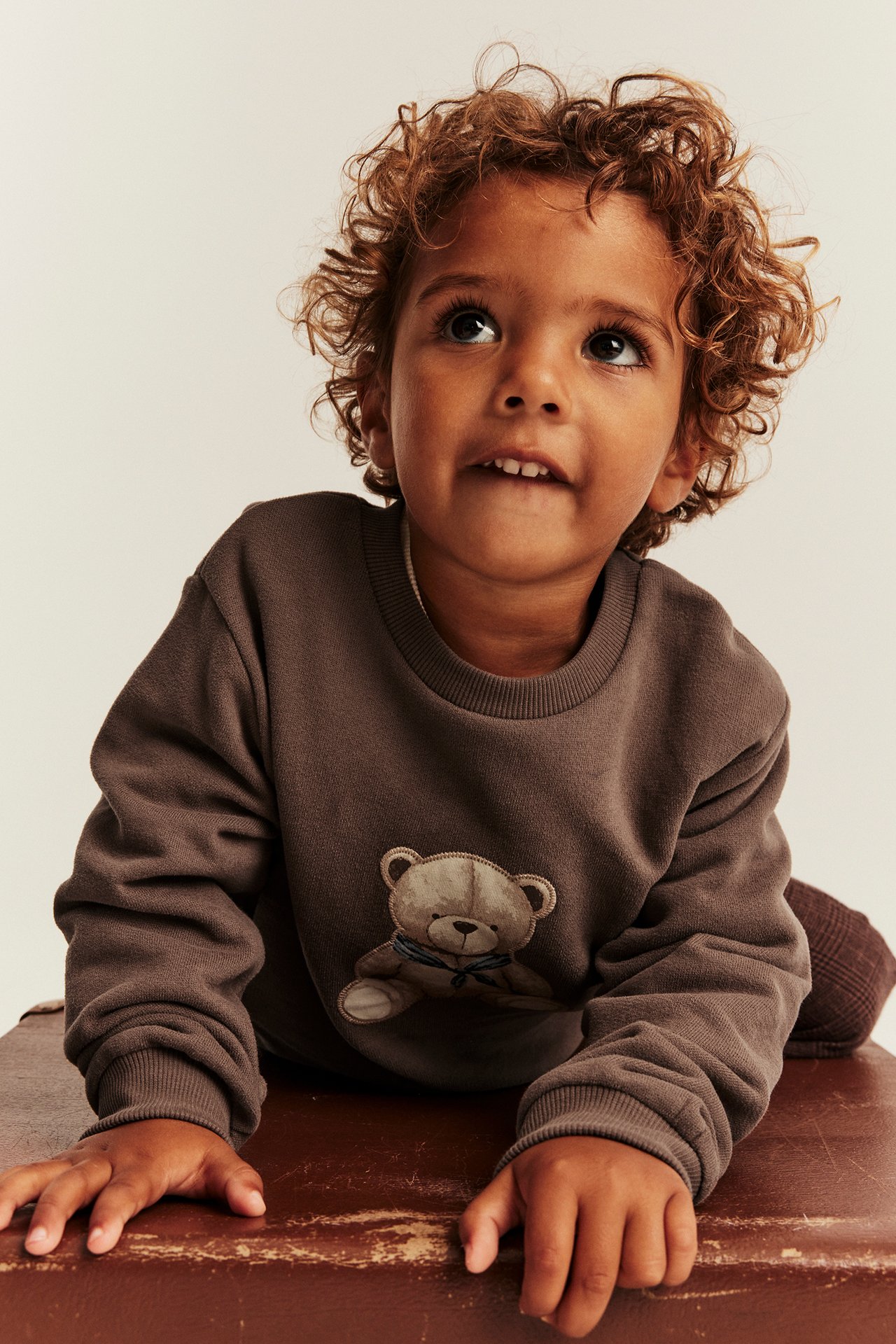 Vorderansicht eines Kindes in dunkelbraunem Langarm-Sweatshirt mit Teddybär-Stickerei.