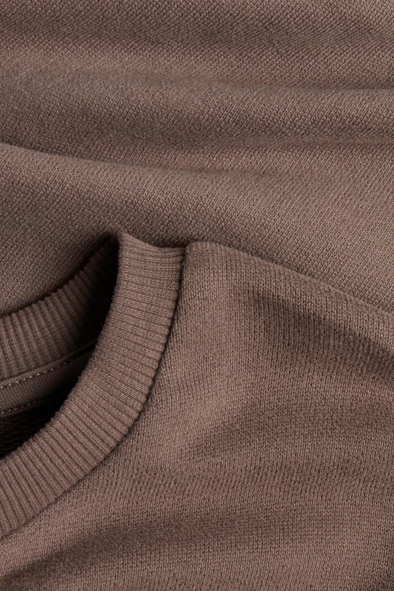 Nahaufnahme eines braunen Langarmshirts mit geripptem Rundhals und Jersey-Textur.
