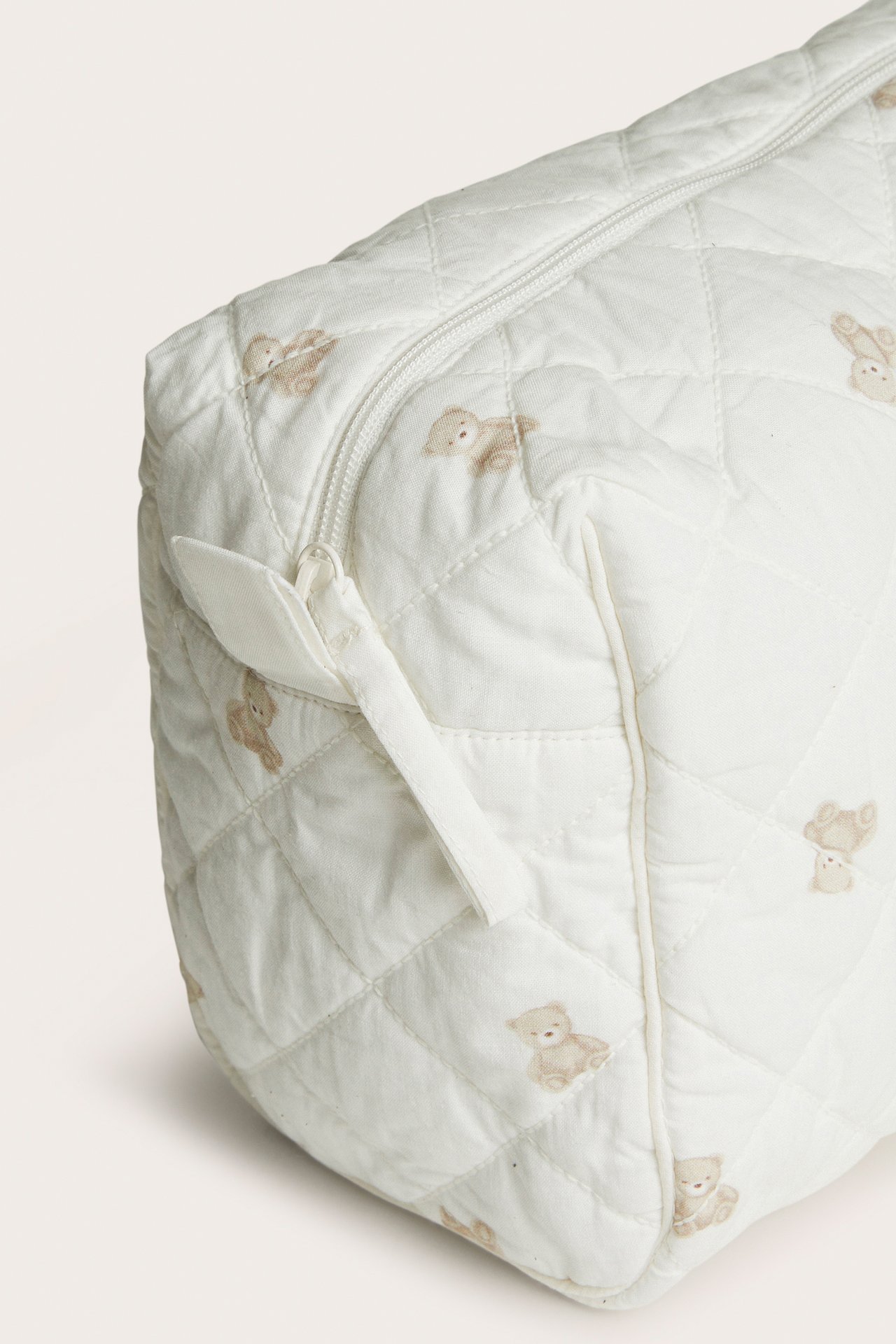 Close-up of a cream quilted fabric bag with teddy bear print and a zipper closure.