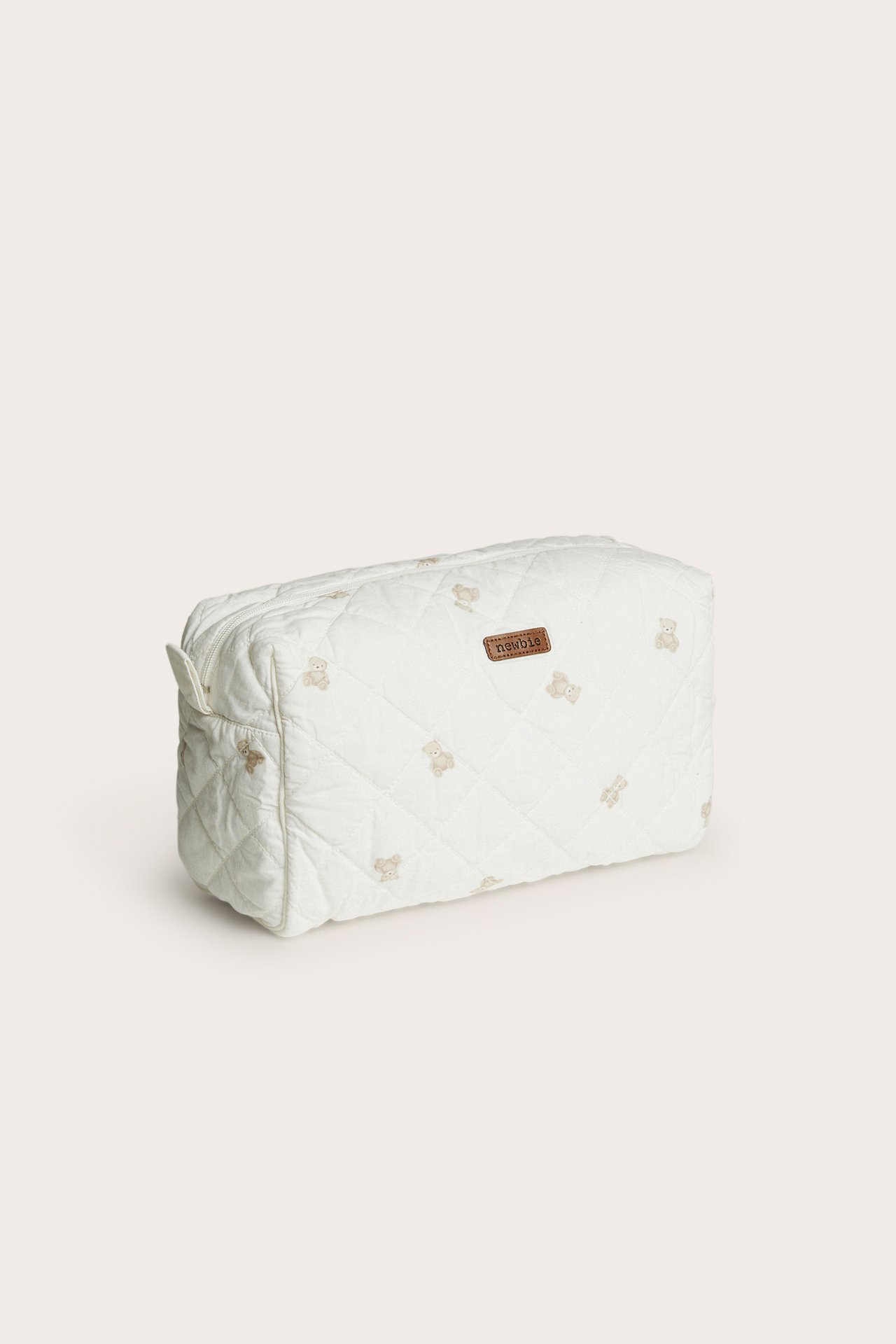 Three-quarter view of a cream quilted pouch with teddy bear embroidery and a 'newbie' label.