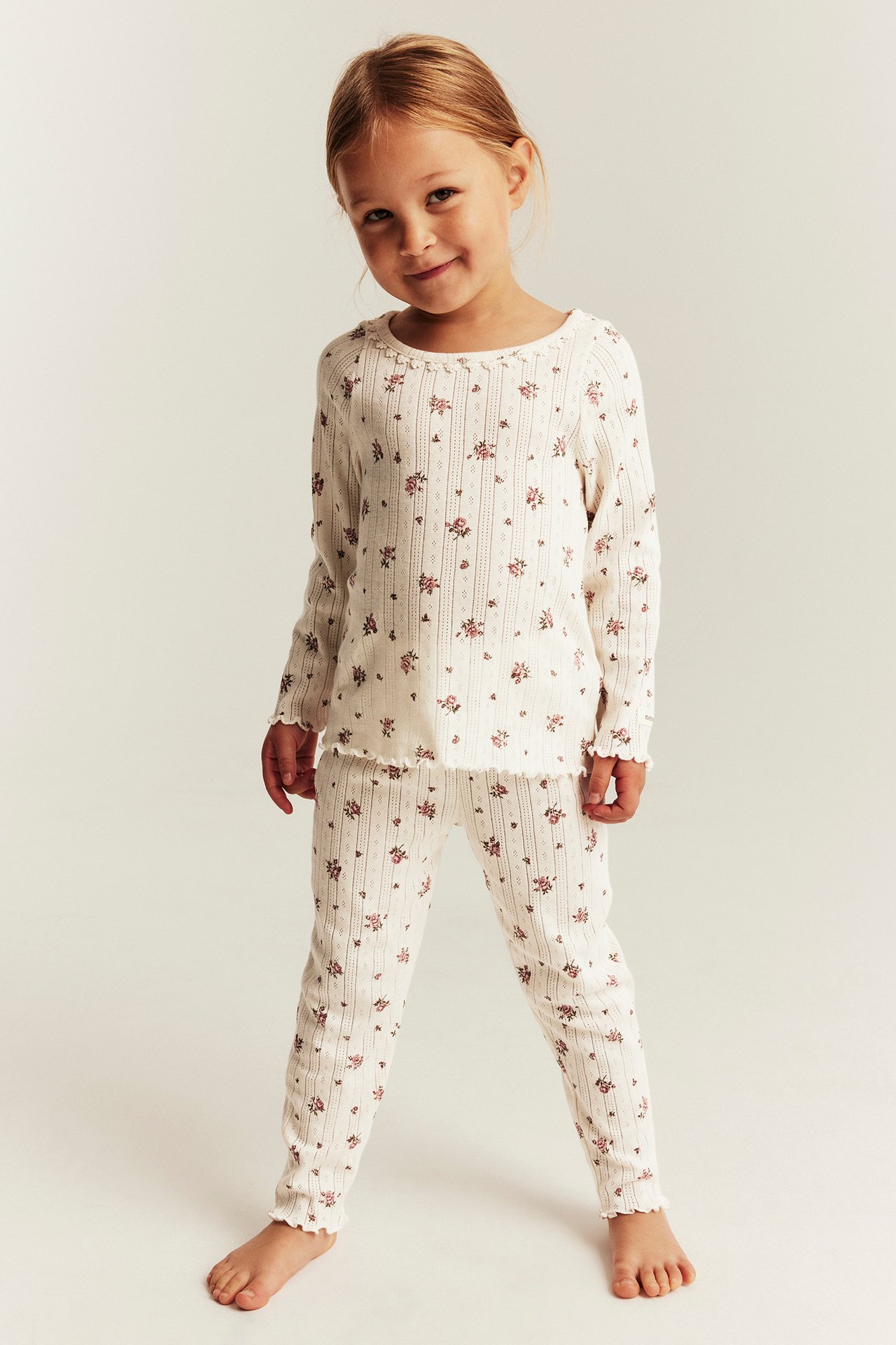 Front view of kid wearing off-white ribbed long-sleeved top and matching pants with floral print.