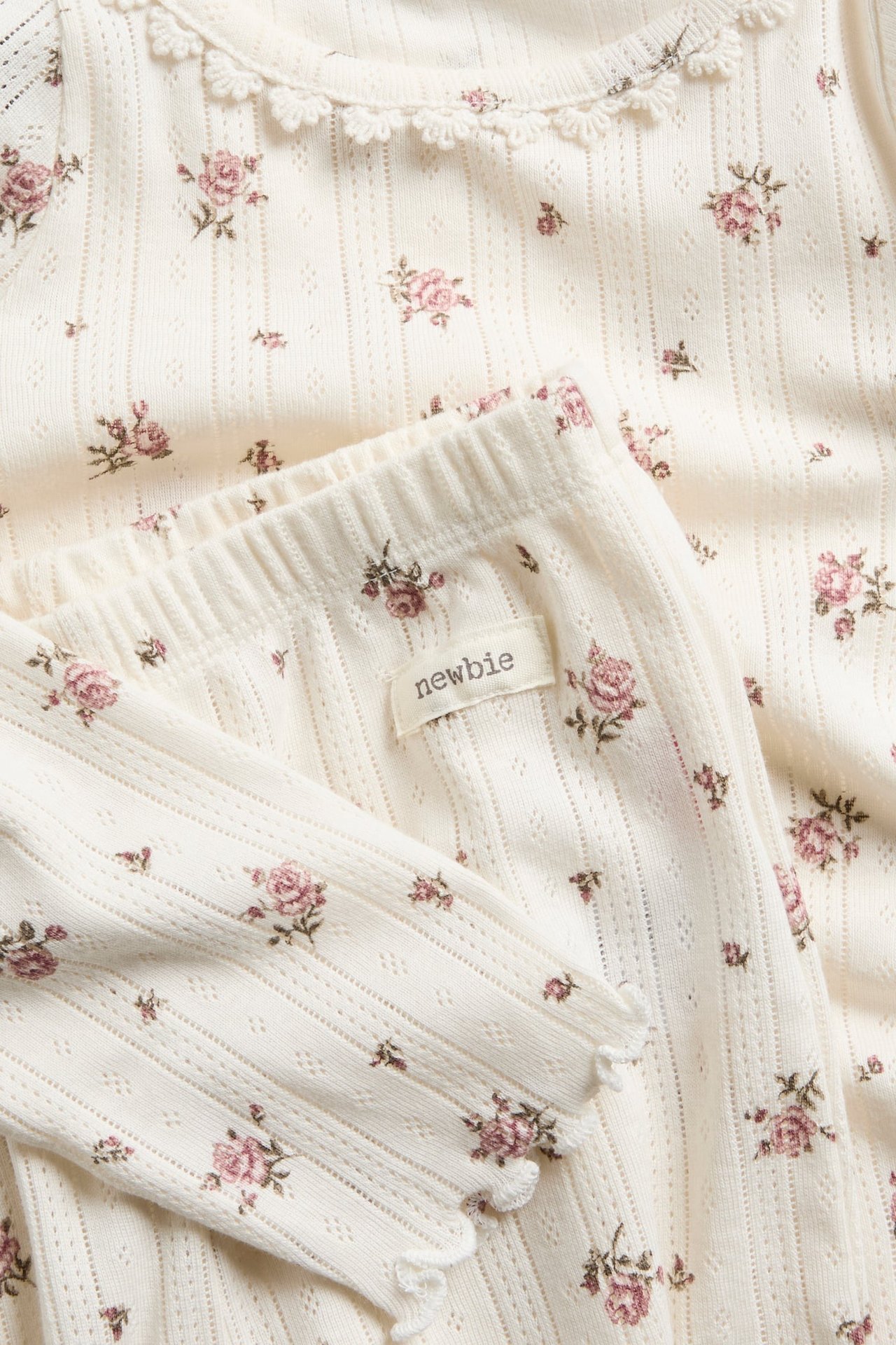 Nahaufnahme eines Baby-Sets aus cremefarbenem Pointelle mit Blumenmuster, Oberteil und Hose mit Spitze.