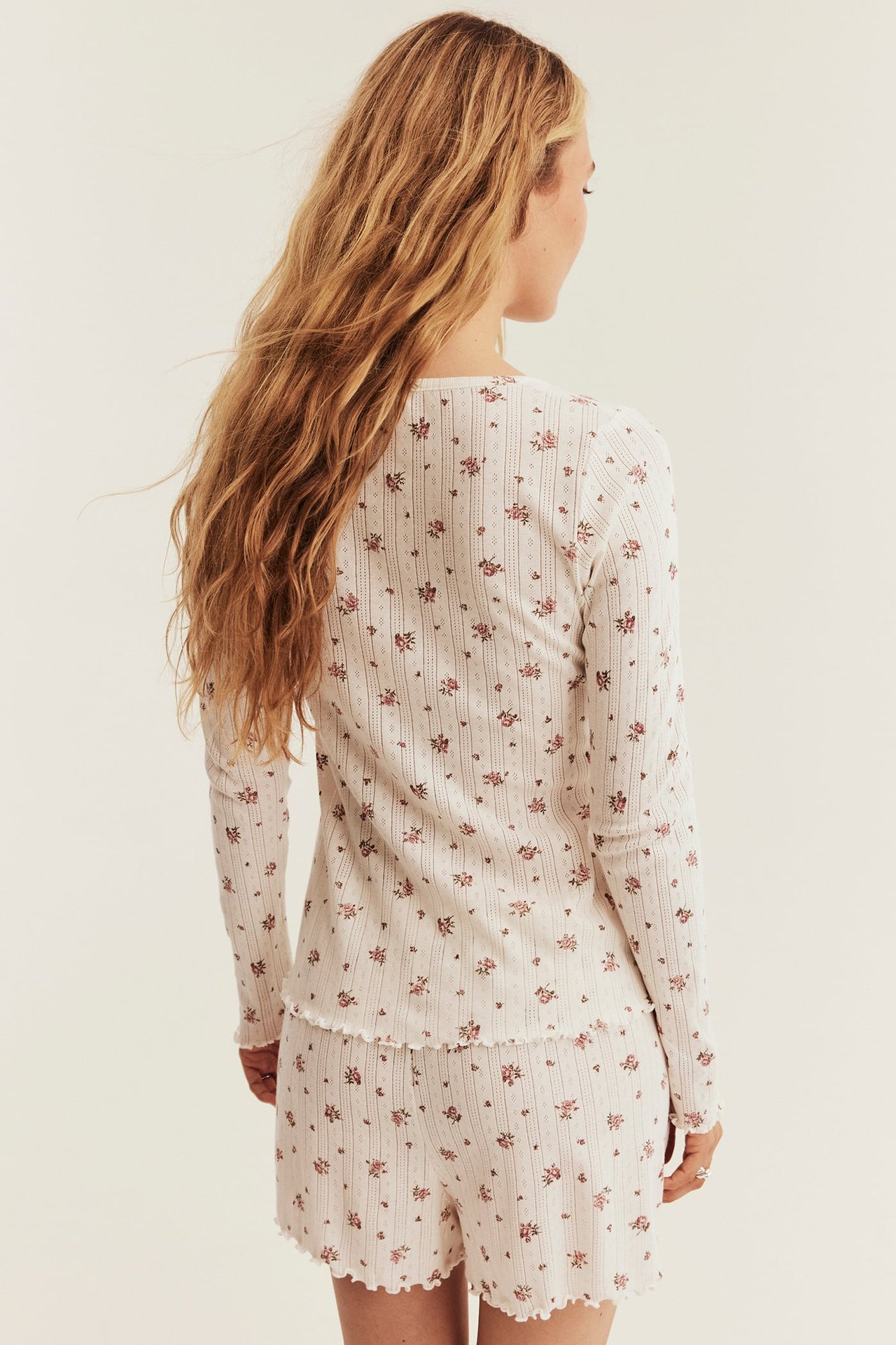 Back view of a woman wearing a white ribbed floral pajama set with ruffled hems.