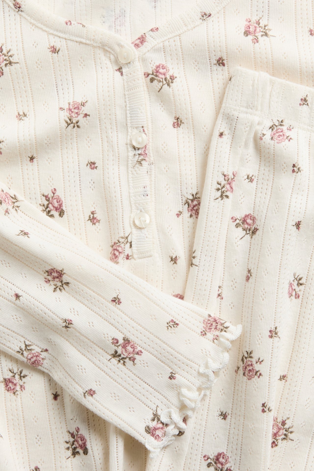 Close-up of a cream floral long-sleeve henley top with matching ribbed pants and ruffled cuffs.