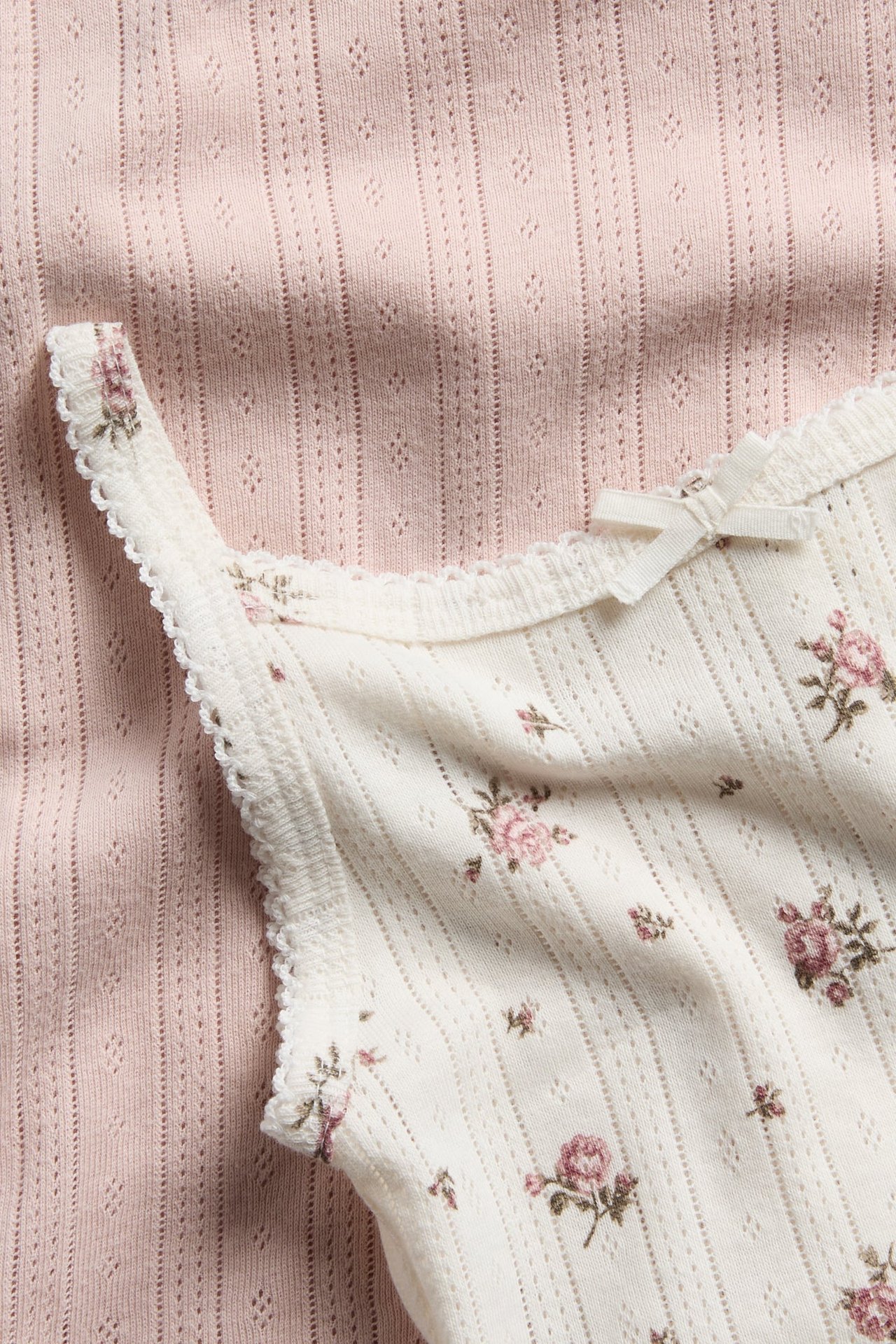Nahaufnahme eines cremefarbenen Blumen-Trägertops mit Spitze und eines rosa Trägertops.