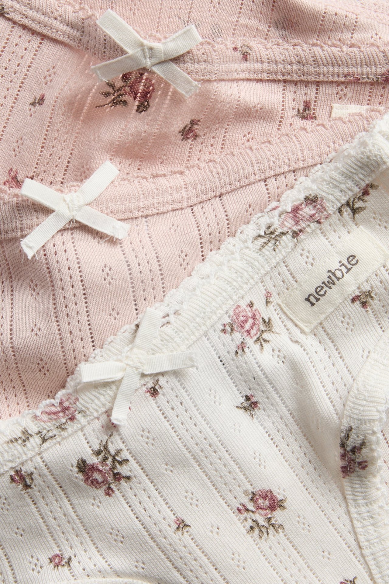 Nahaufnahme von weißer und rosa Babyunterwäsche mit Blumenmuster, Lochmuster und kleinen Schleifen.