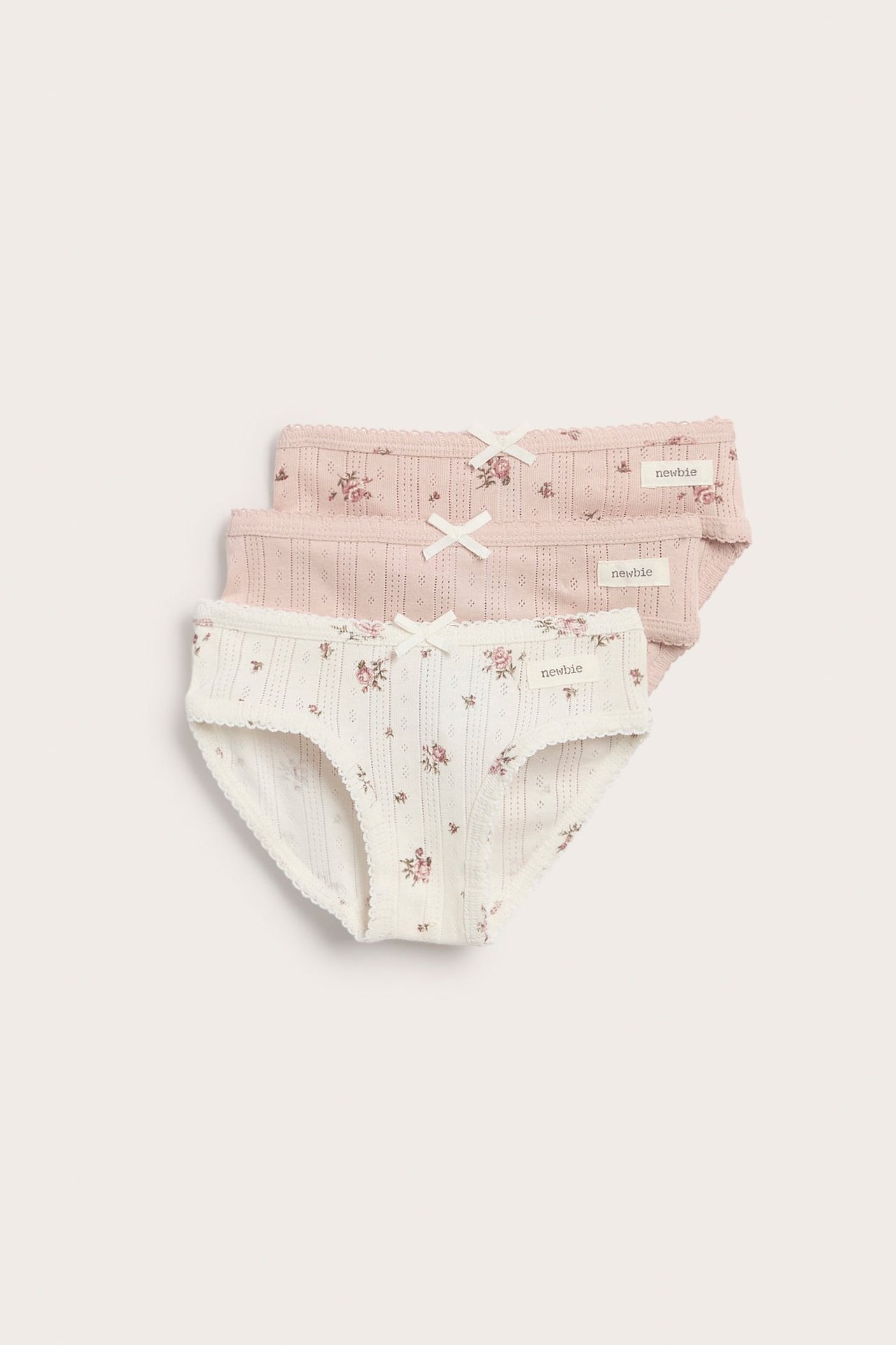 Drei Kinderunterhosen, eine weiße und zwei rosafarbene, mit Blumenmuster, Lochstickerei und kleinen weißen Schleifen.
