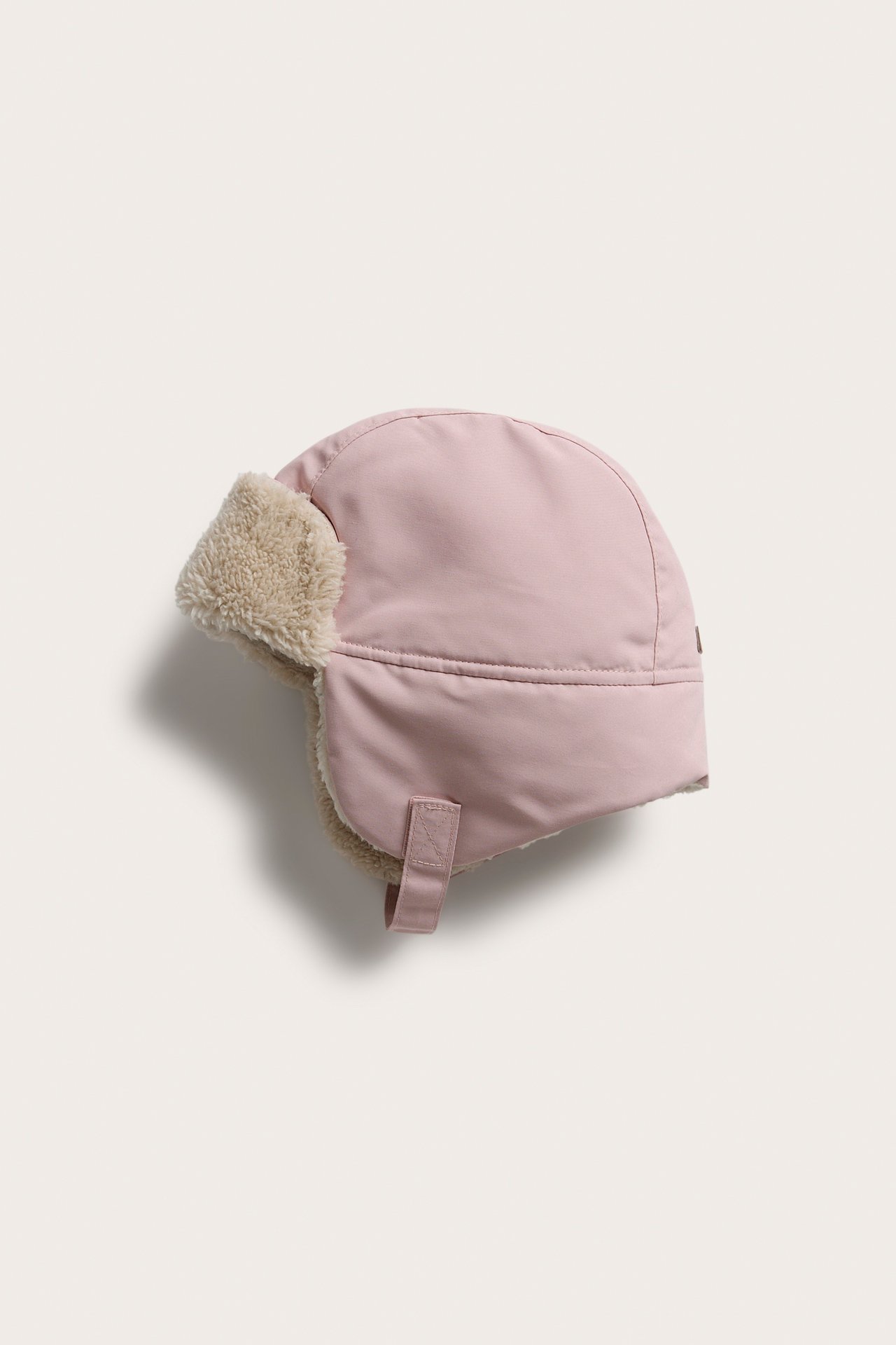 Seitenansicht einer rosa Pilotenmütze mit beigem Kunstfellfutter und Kinnriemen.