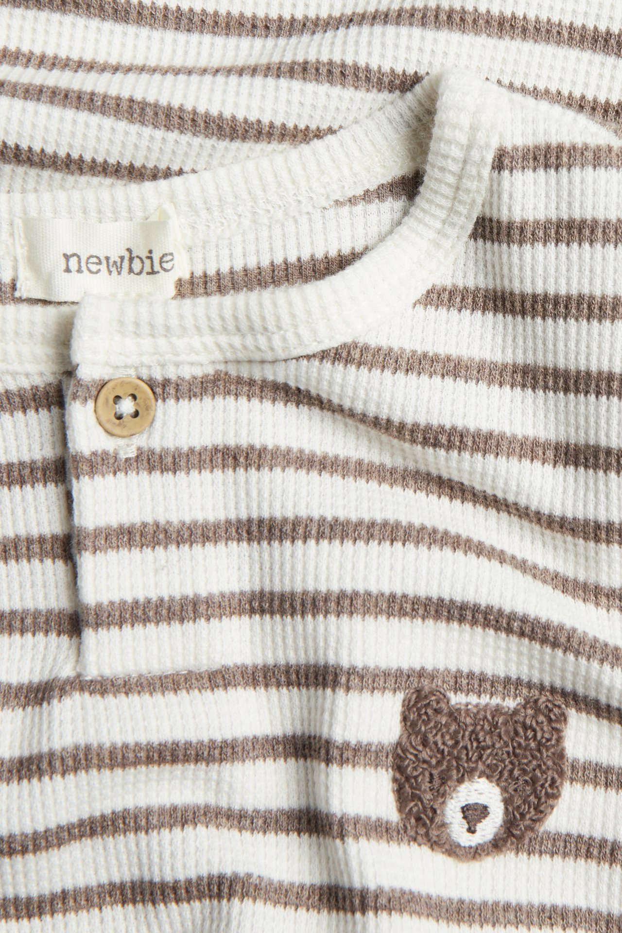Close-up of a baby's white and brown striped waffle knit top with a wooden button and bear embroidery.