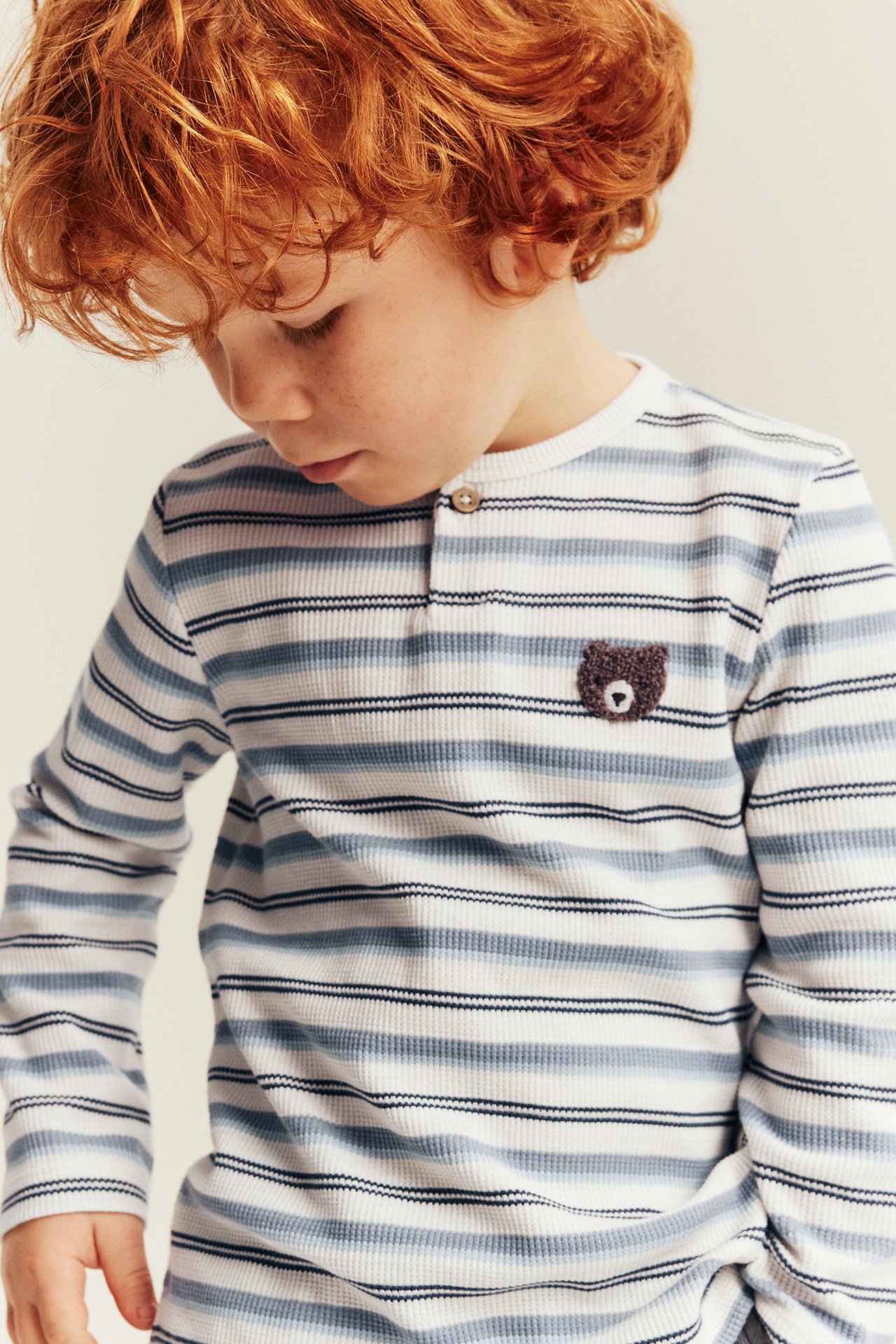 Front view of a kid wearing a white and blue striped long-sleeve Henley shirt with a bear patch.