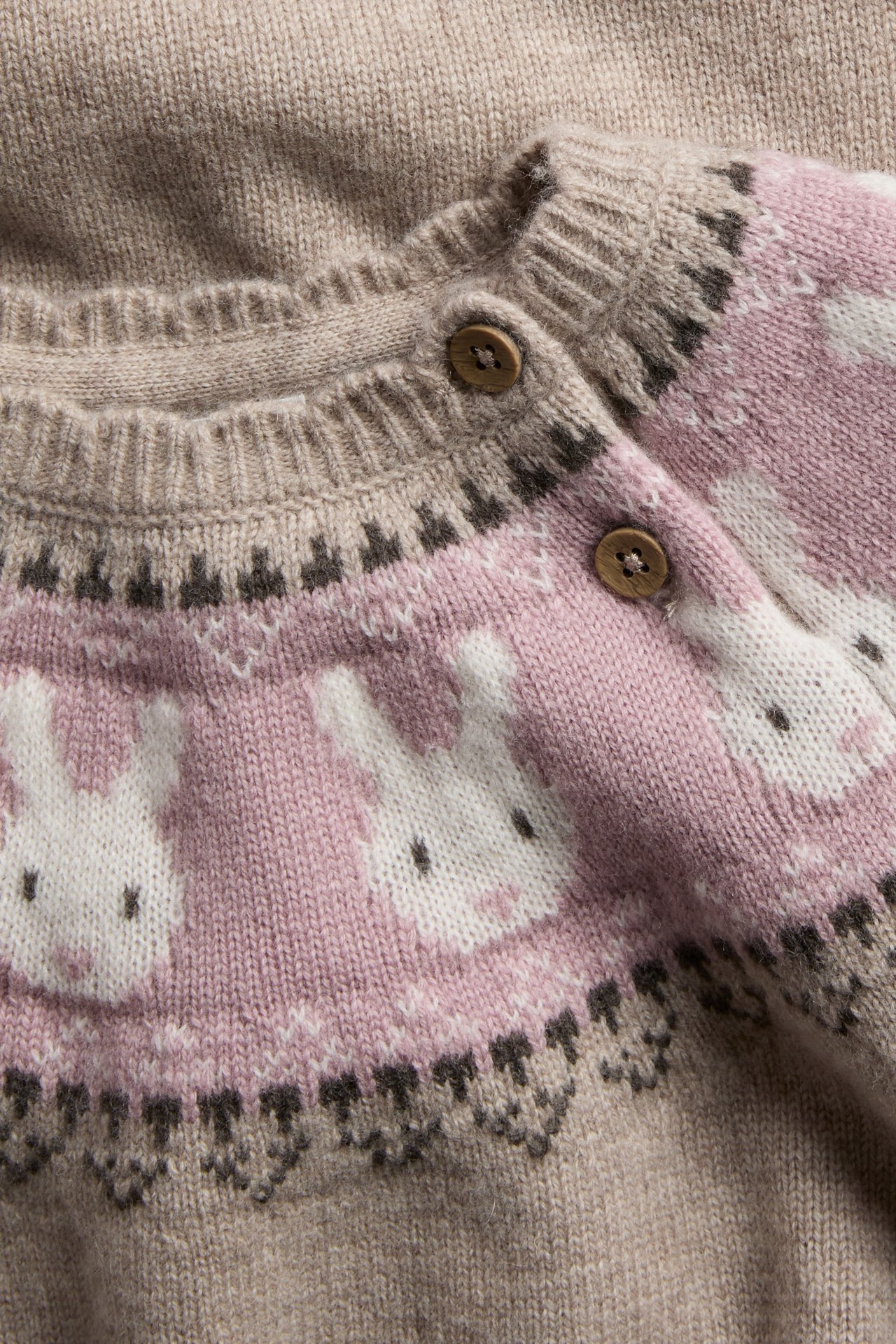Nahaufnahme einer beigen Strickbabyjacke mit rosa, weißem und braunem Hasenmuster und Holzknöpfen.