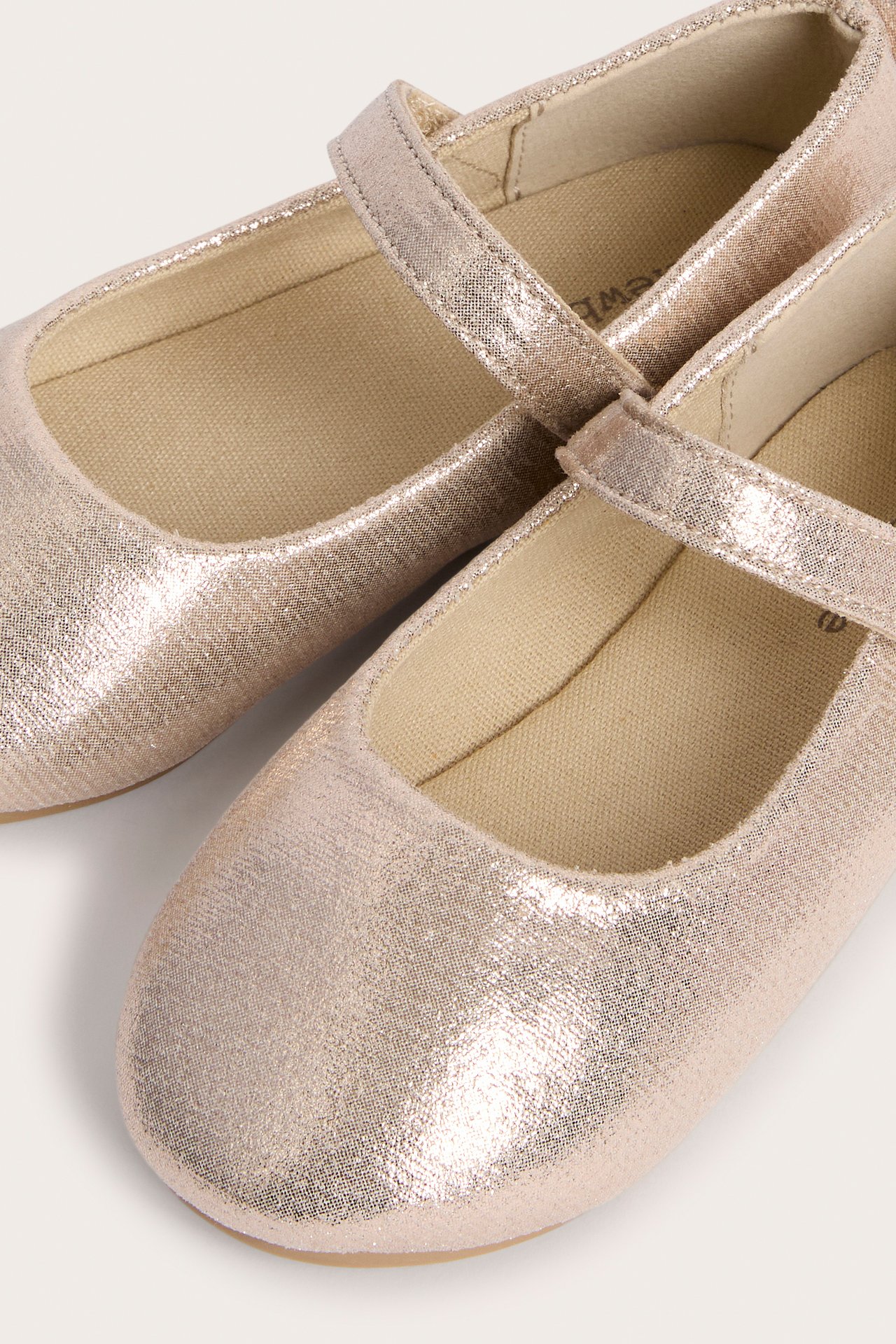 Nahaufnahme von roségoldenen glitzernden Mary Jane-Ballerinas für Kinder mit beiger Innensohle.