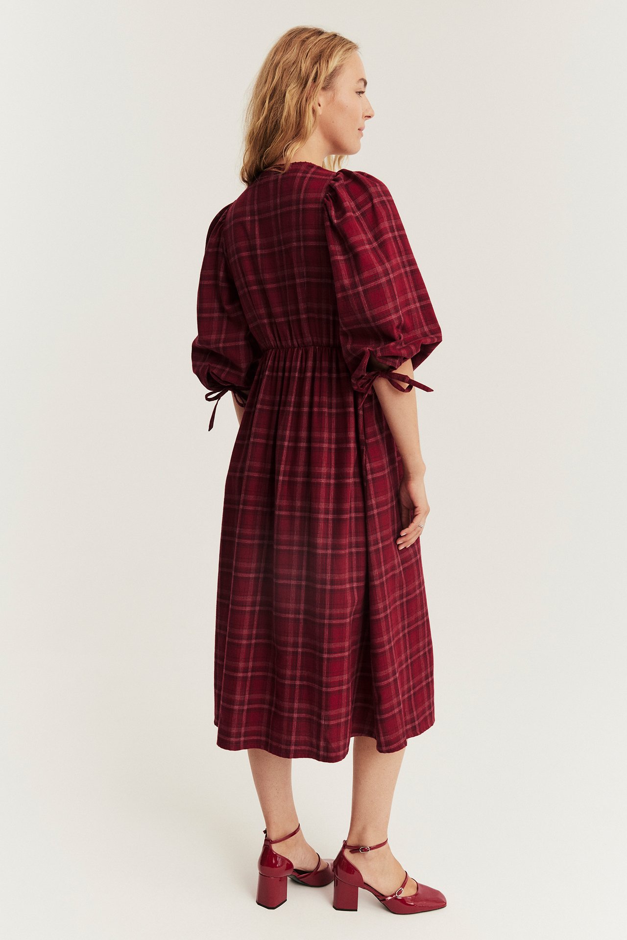 Frau von hinten: rotes kariertes Midikleid mit Puffärmeln und roten Lack-Blockabsatzschuhen.