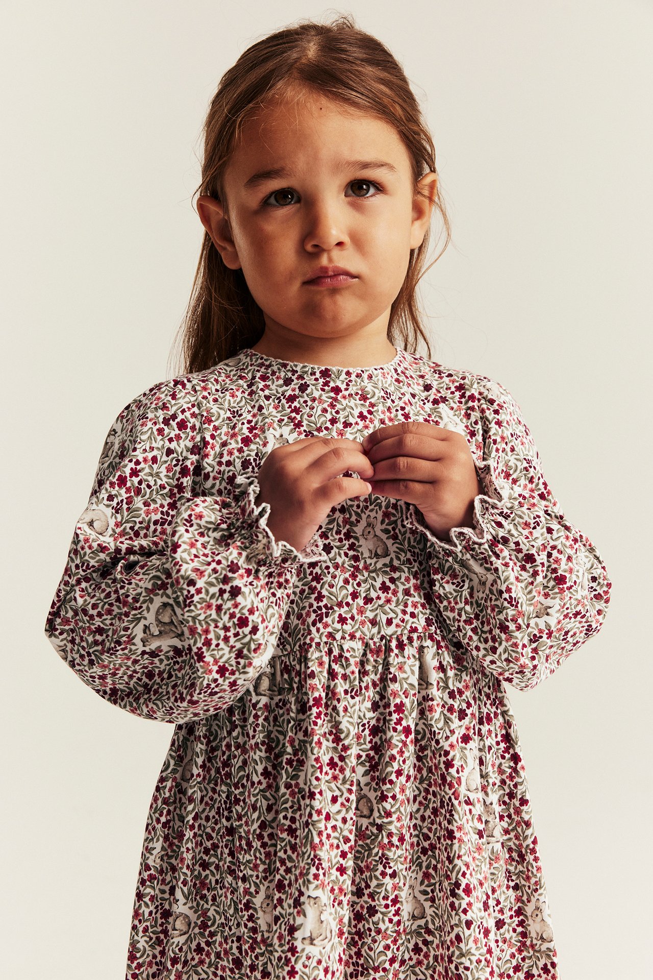 Front view of a kid girl wearing a white floral and rabbit pattern long-sleeved dress with ruffled cuffs.