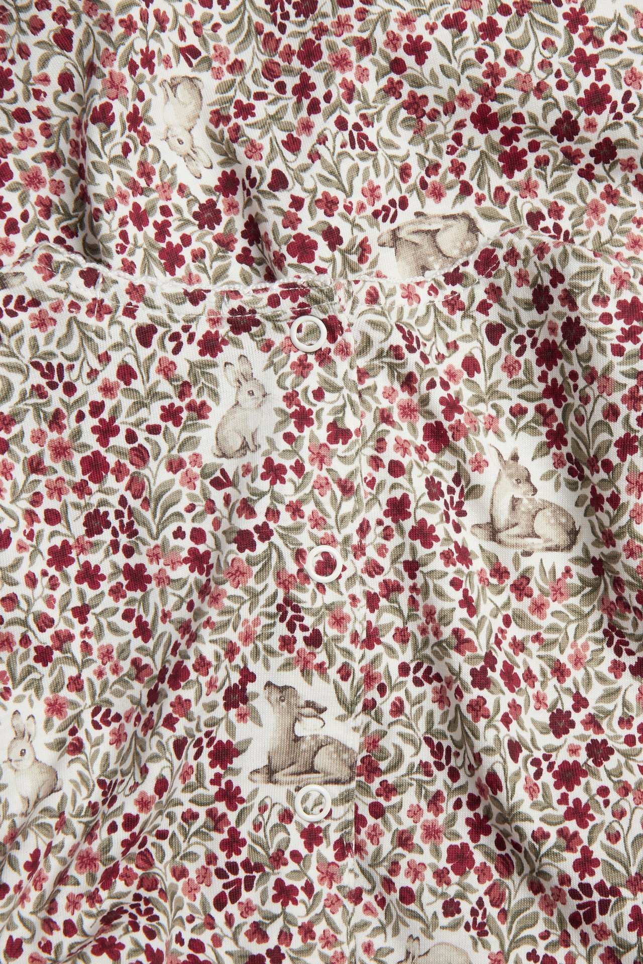 Close-up of a white ribbed baby garment with red floral and animal print, featuring white snap buttons.
