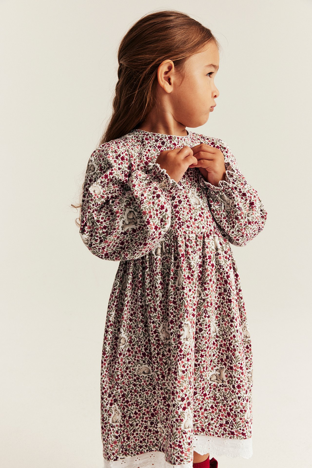 Side view of kid in white floral, bunny print long-sleeved dress with lace trim.