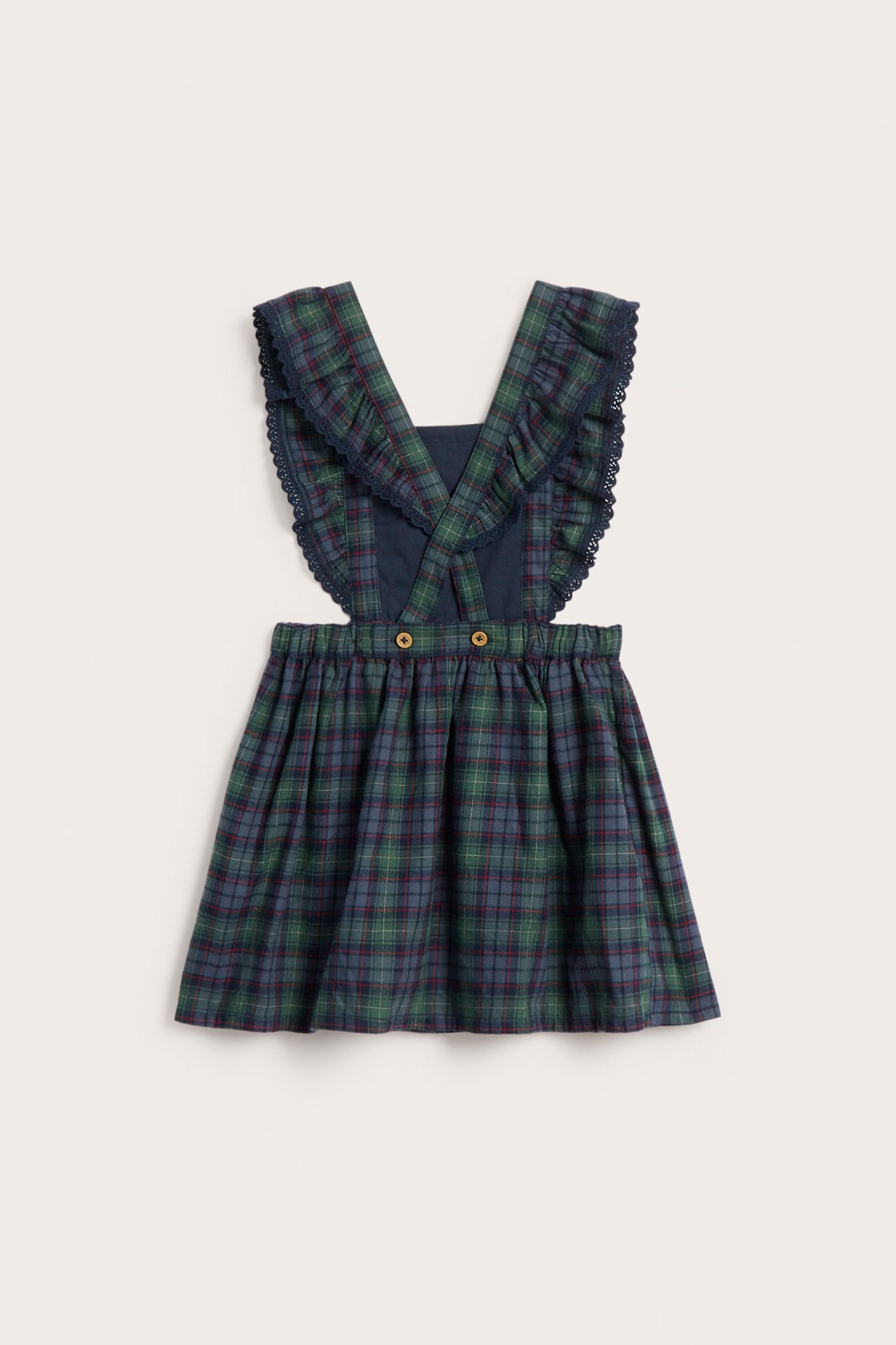 Front view of a kid's green and blue plaid pinafore dress with ruffled navy straps and two buttons.