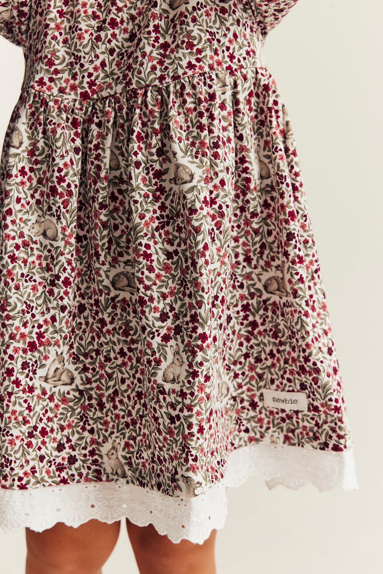Nahaufnahme eines cremefarbenen Kinderkleides mit rotem Blumen- und Waldtiermuster und weißer Spitzenborte.