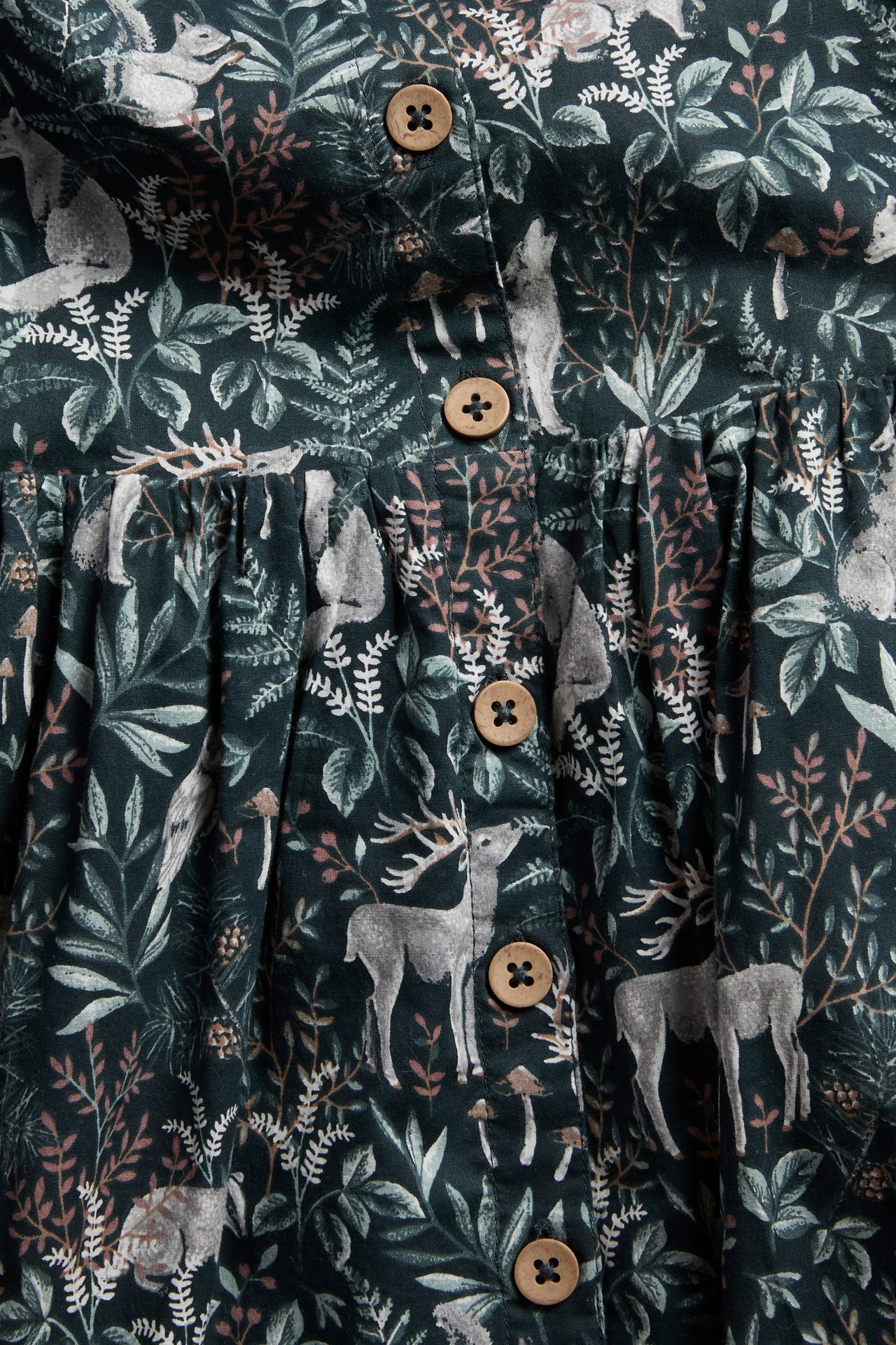 Close-up of a dark green garment with a forest animal print, featuring light brown wooden buttons.