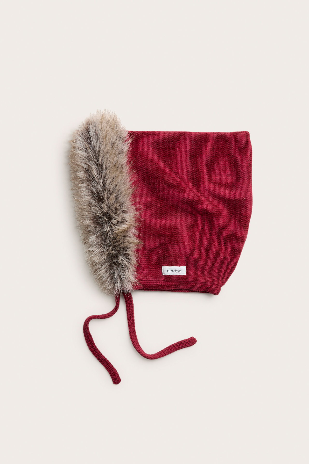 Vorderansicht einer roten gestrickten Babyhaube mit Kunstpelzbesatz und Bindebändern.