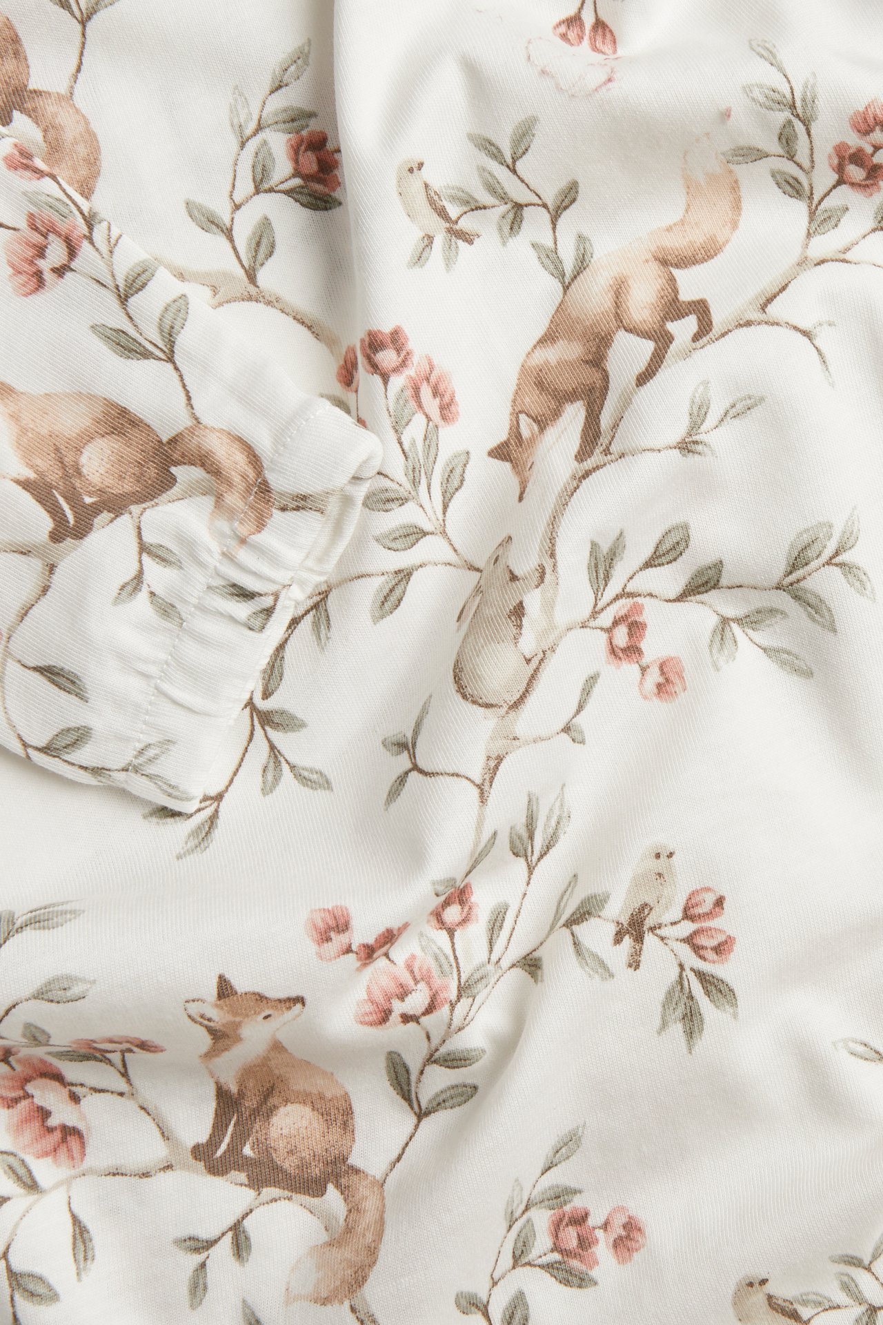Nahaufnahme eines cremefarbenen Kleidungsstücks mit Fuchs-, Vogel- und rosa Blumendruck und Rüschenmanschette.