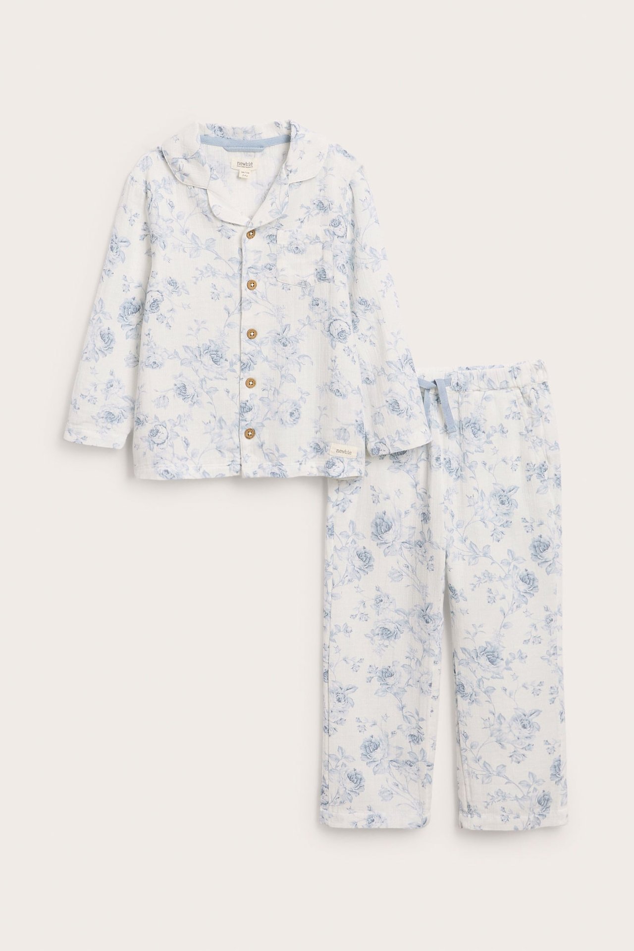 Vorderansicht eines weißen Kinder-Baumwollpyjamas mit blauem Blumenmuster, Hemd mit Knöpfen und Hose mit Kordelzug.