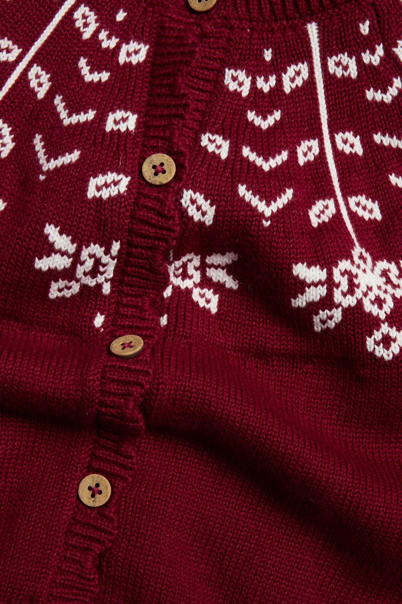 Close-up of a dark red knitted cardigan with white snowflake patterns and wooden buttons.