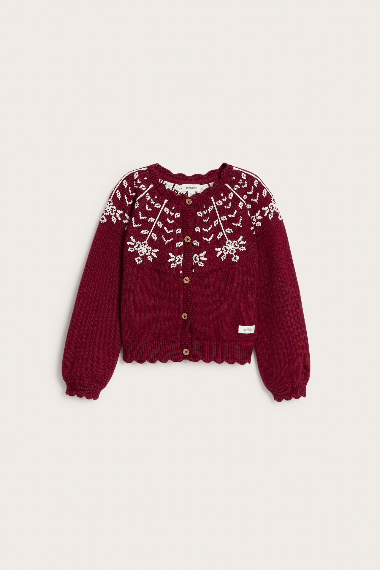 Front view of a kid's burgundy knit cardigan with white snowflake pattern, scalloped edges, and button fastening.