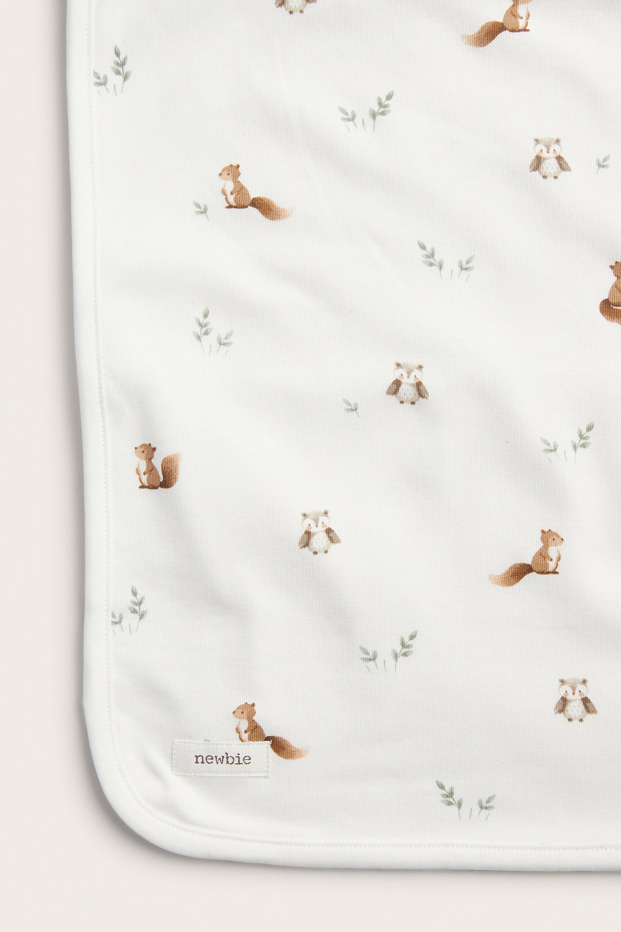 Nahaufnahme einer weißen Babydecke mit braunem Eichhörnchen- und Eulenmuster.