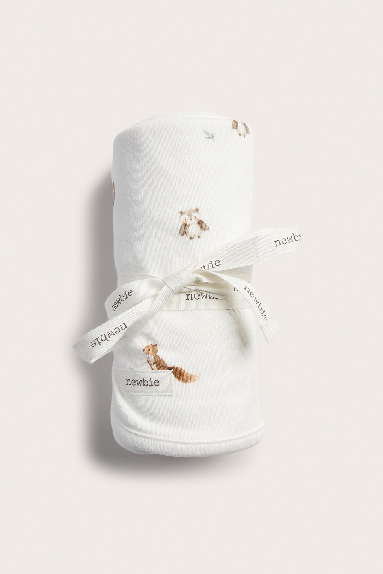 Vorderansicht einer gerollten weißen Babydecke mit Tiermotiven und 'newbie'-Band.