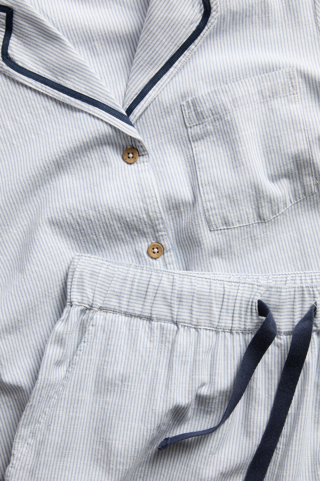 Close-up: blue and white striped cotton pajama top with wooden buttons, chest pocket, and matching drawstring pants.