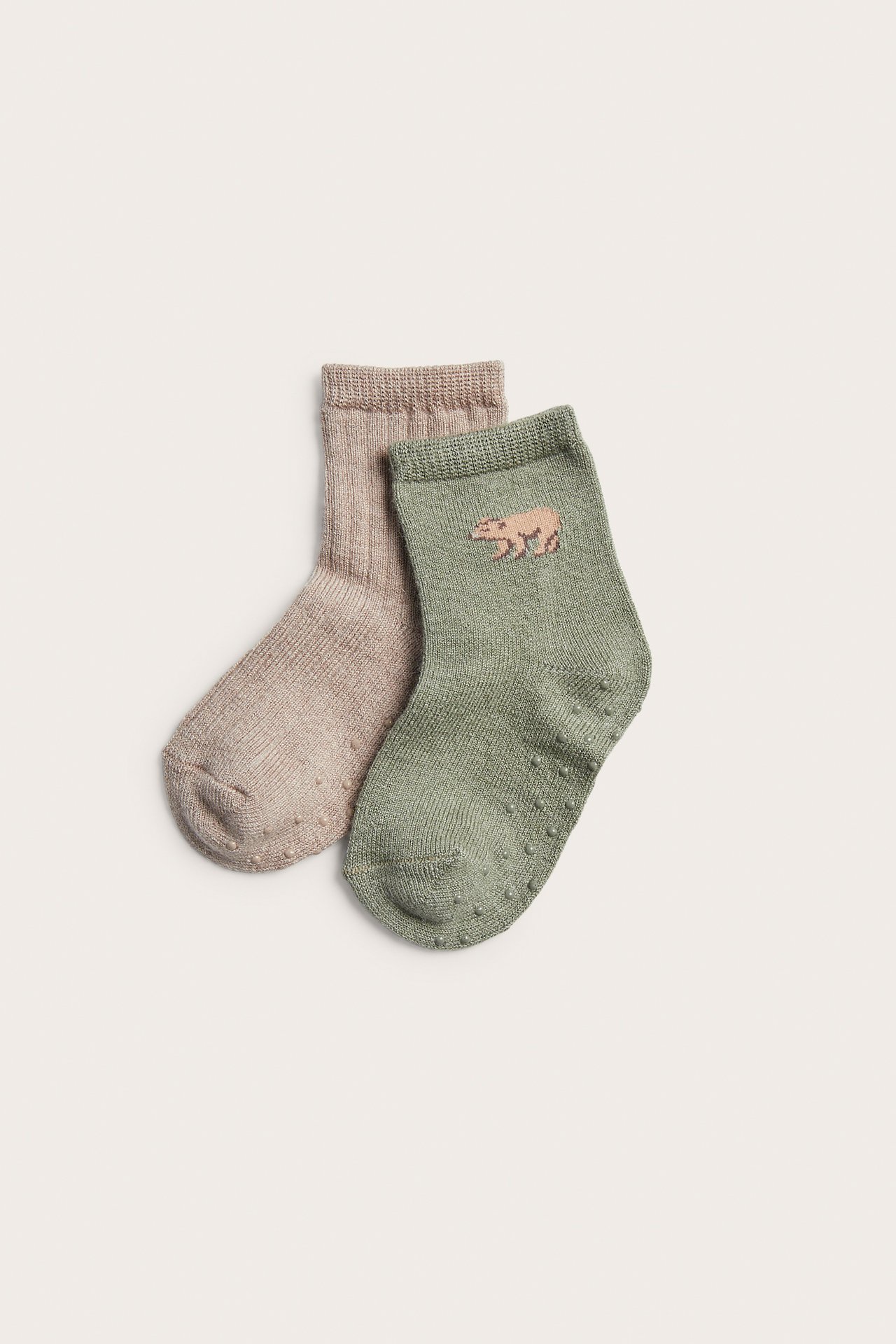 Eine grüne Babysocke mit Bärenstickerei und Antirutsch-Noppen, und eine beige Babysocke.