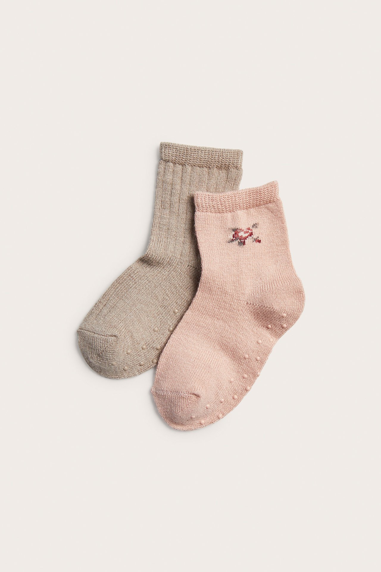 Draufsicht: rosa Babysocke mit Blumenstickerei und taupe gerippte, beide mit Anti-Rutsch-Sohle.