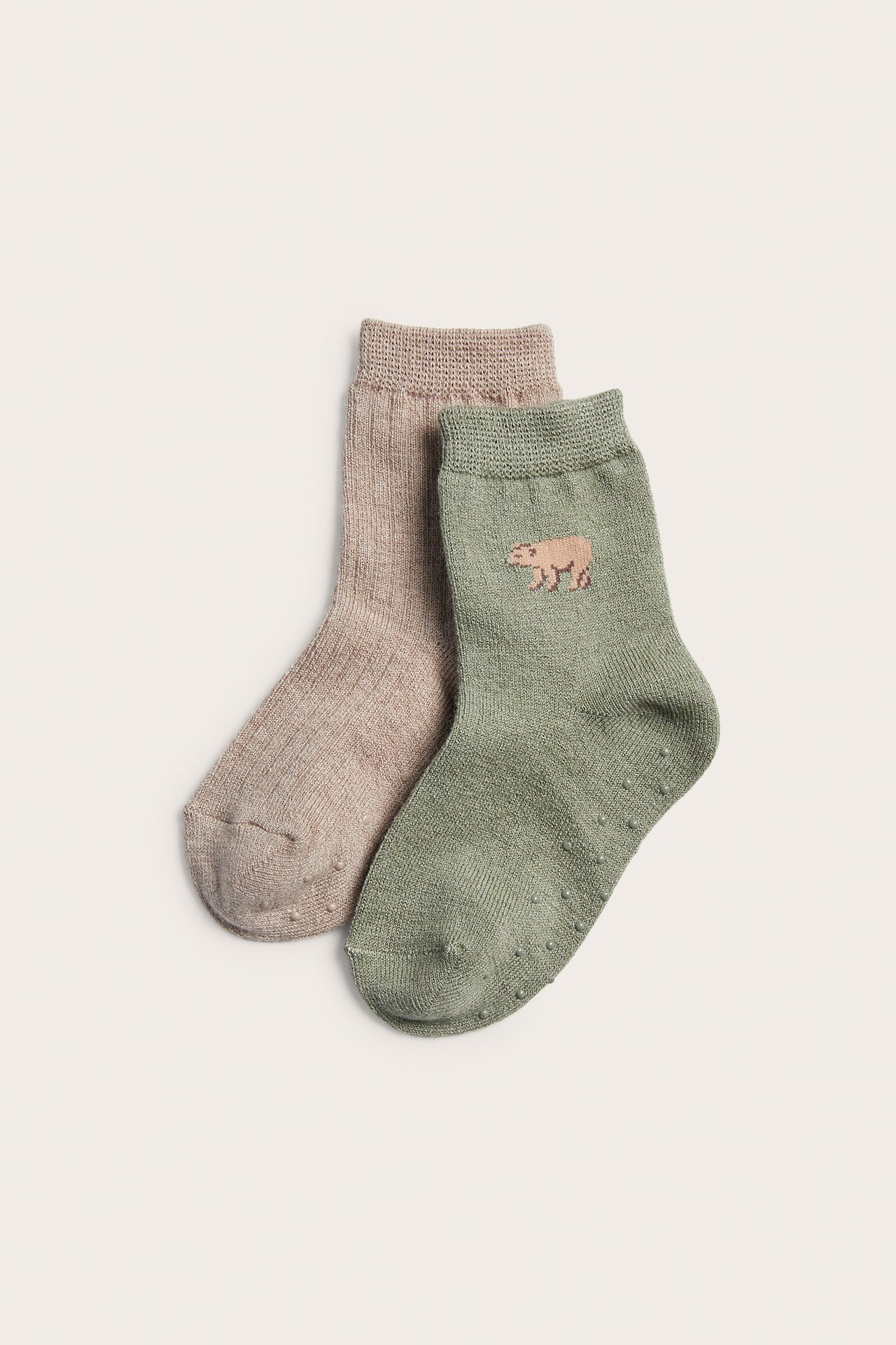 Zwei Paar rutschfeste Babysocken: ein salbeigrünes mit Tierstickerei, ein hellbraunes.