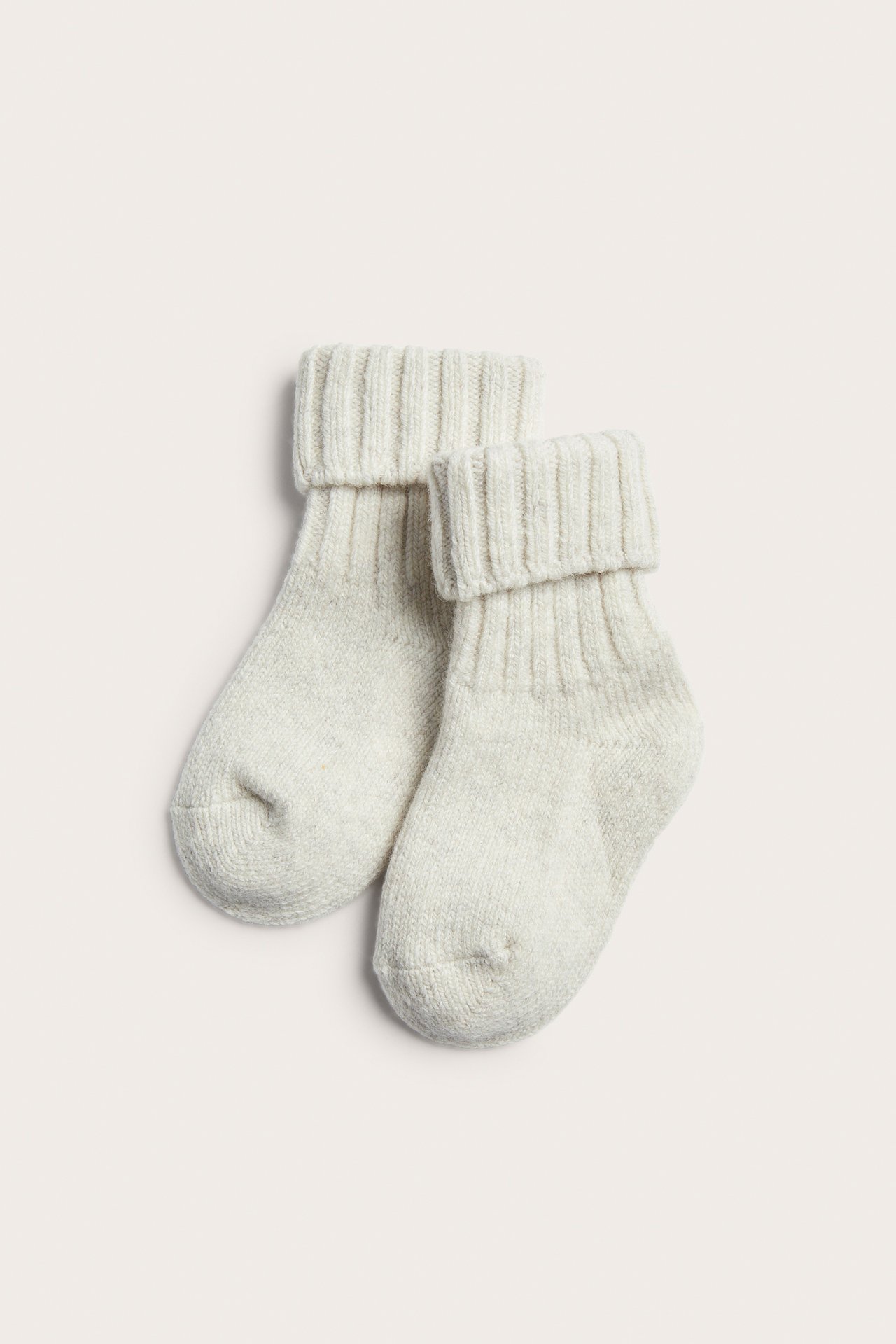 Top view of a pair of light beige knitted baby socks with ribbed cuffs.