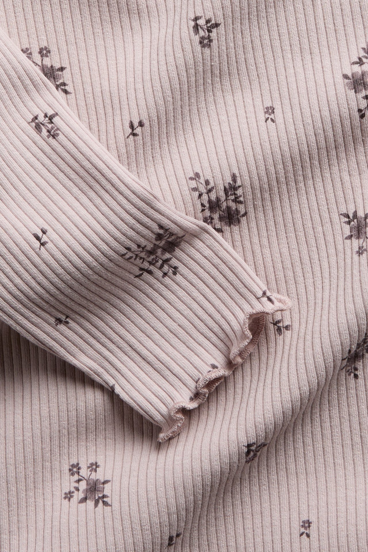Nahaufnahme eines hellrosa gerippten Langarmshirts mit dunklem Blumenmuster und Rüschenbündchen.