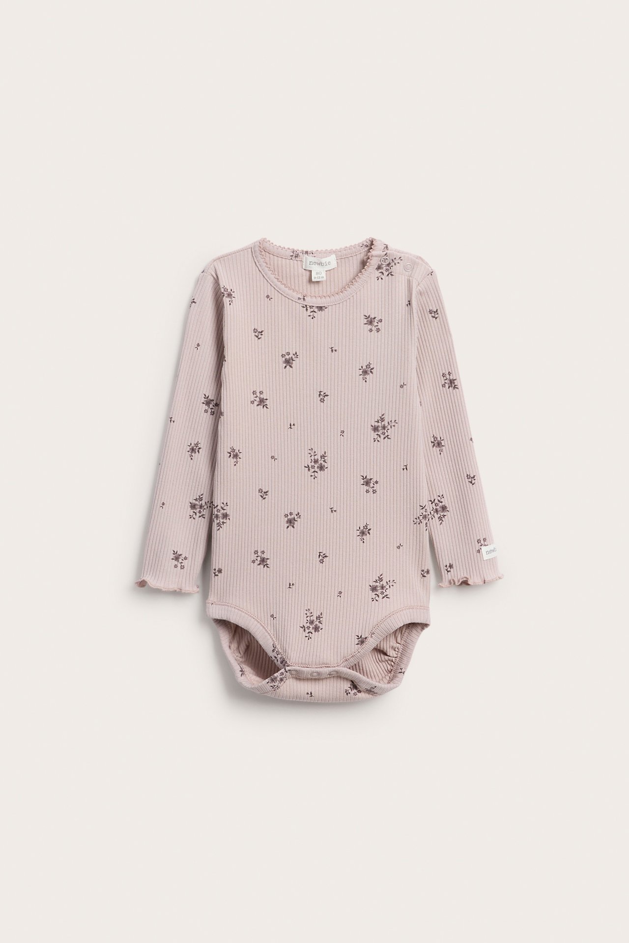 Vorderansicht eines hellrosafarbenen gerippten Langarm-Babybodys mit dunklem Blumenmuster und Rüschensaum.