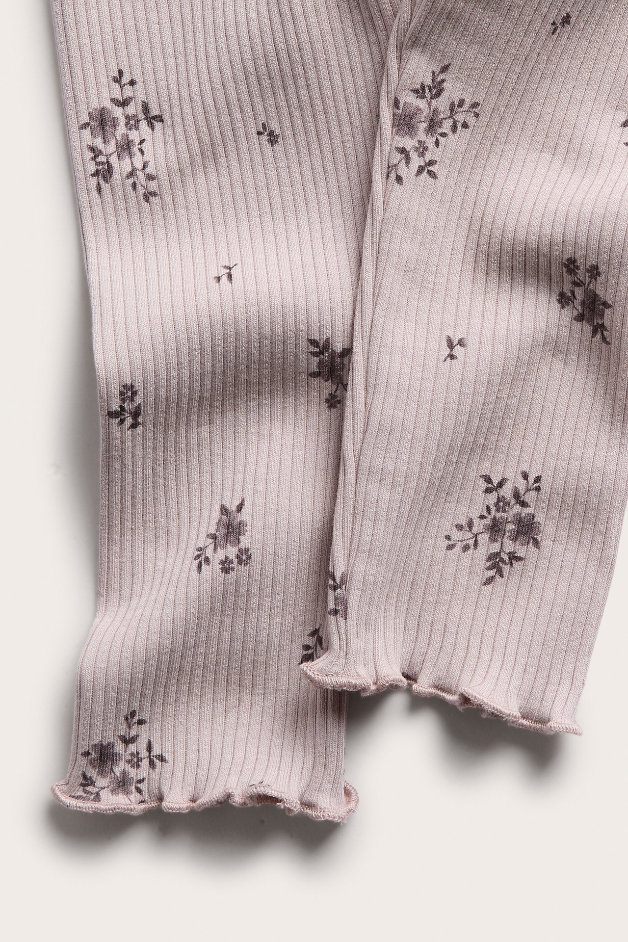 Close-up of a light purple ribbed garment with a dark floral print and ruffled hems.