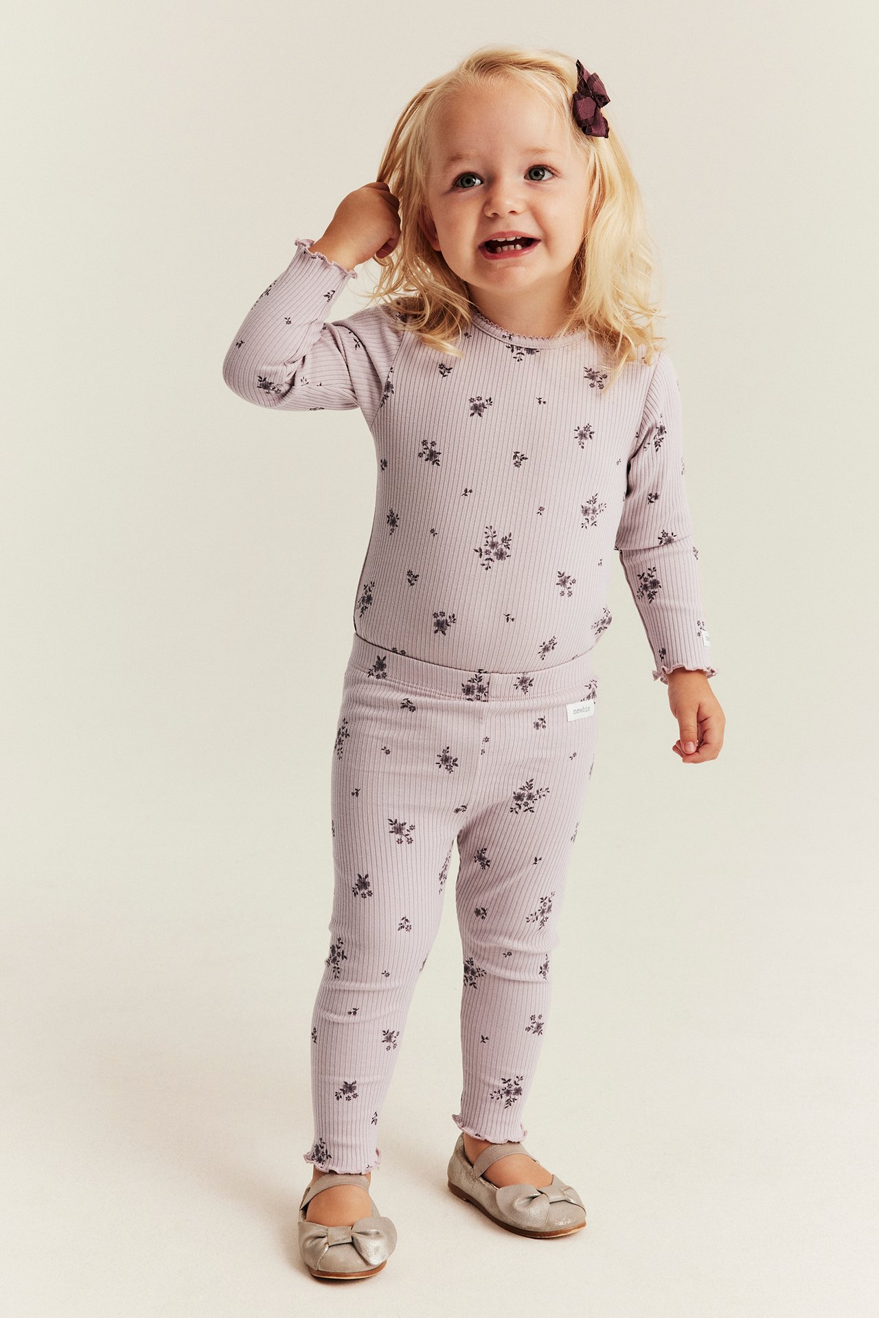Vorderansicht eines zweiteiligen lila Ripp-Loungewear-Sets mit Blumenmuster für Kinder und metallisch-silbernen Ballerinas.