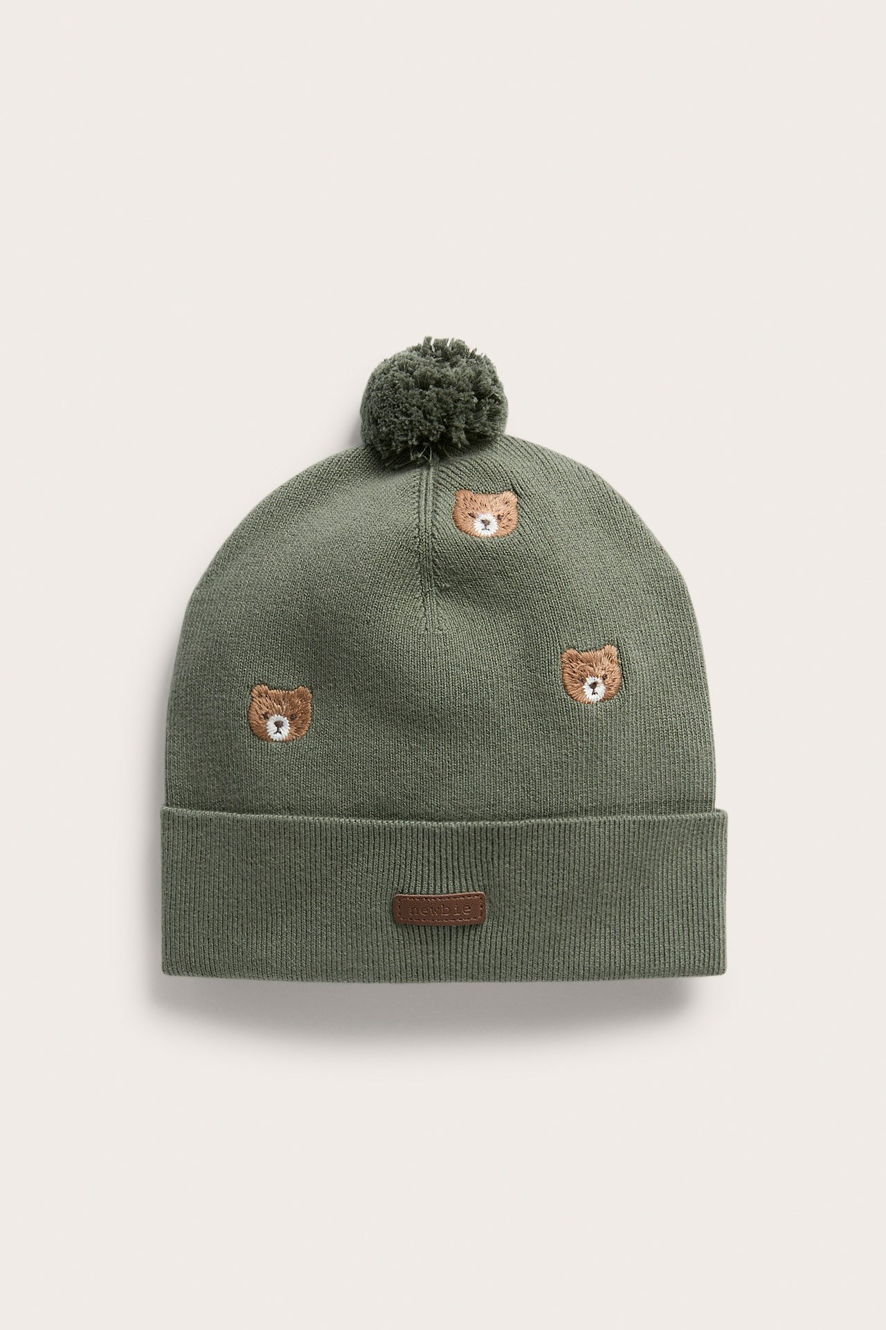 Vorderansicht einer grünen Strickmütze mit Bommel und Bärenstickereien.